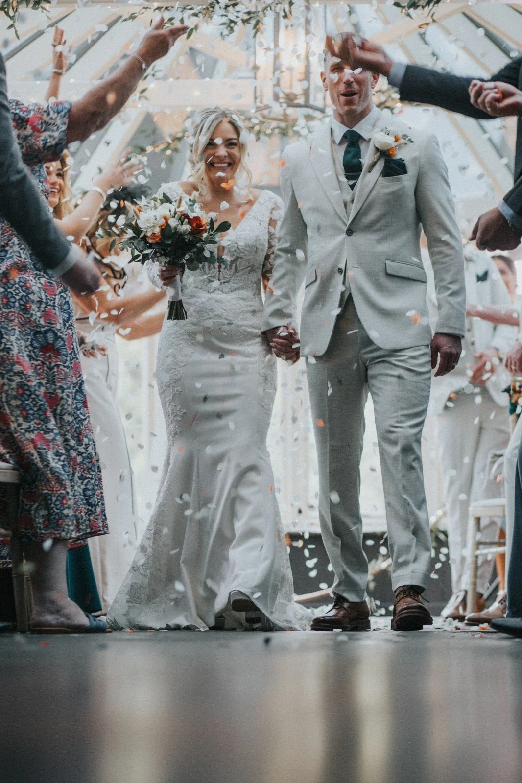 A bride and groom walking hand in hand under a canopy, celebrating their wedding with guests throwing confetti around them.