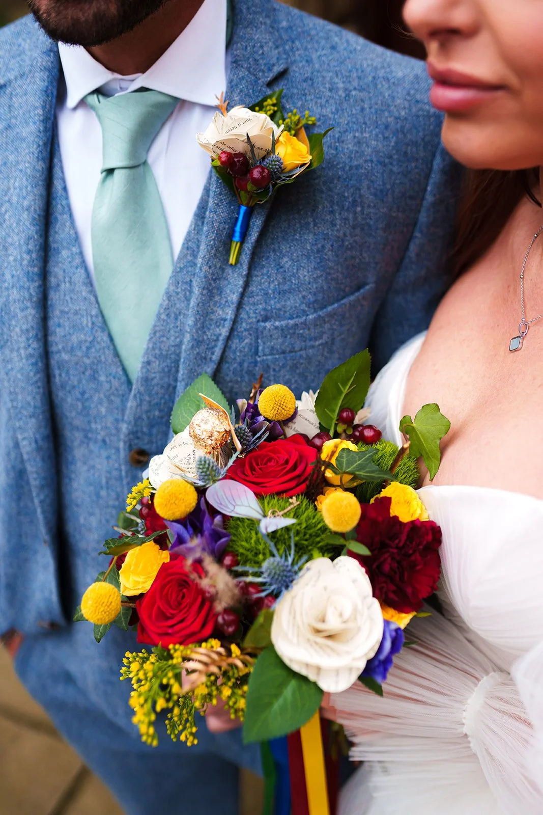 Couple dressed in wedding attire holding a colorful bouquet of flowers, including roses, berries, and greenery.