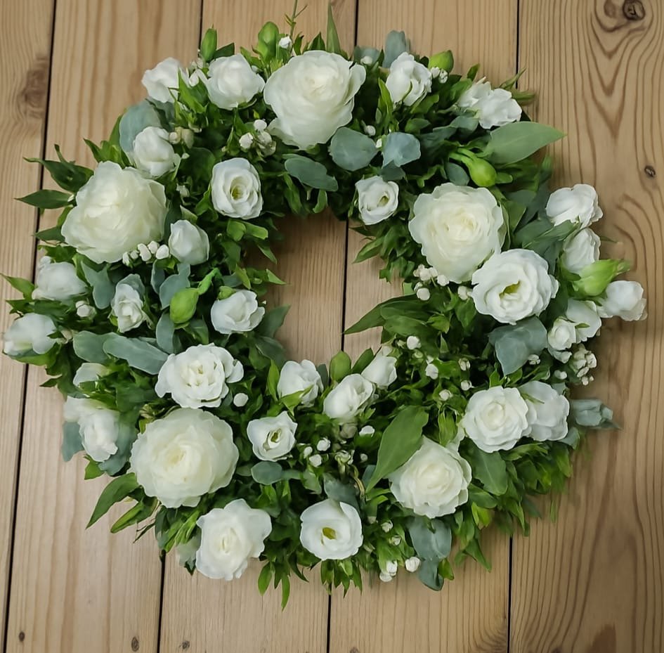 White floral wreath with greenery hanging on a wooden wall.