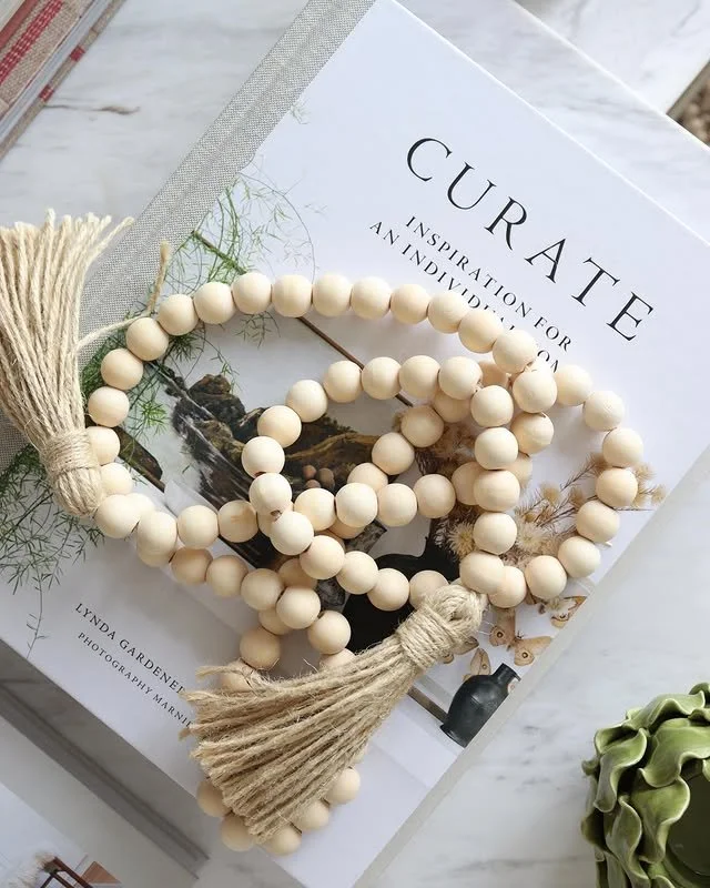 A string of cream-colored wooden bead prayer beads with tassels, resting on a magazine titled 'CURA TE' with an inspirational subtitle, placed on a marble surface.