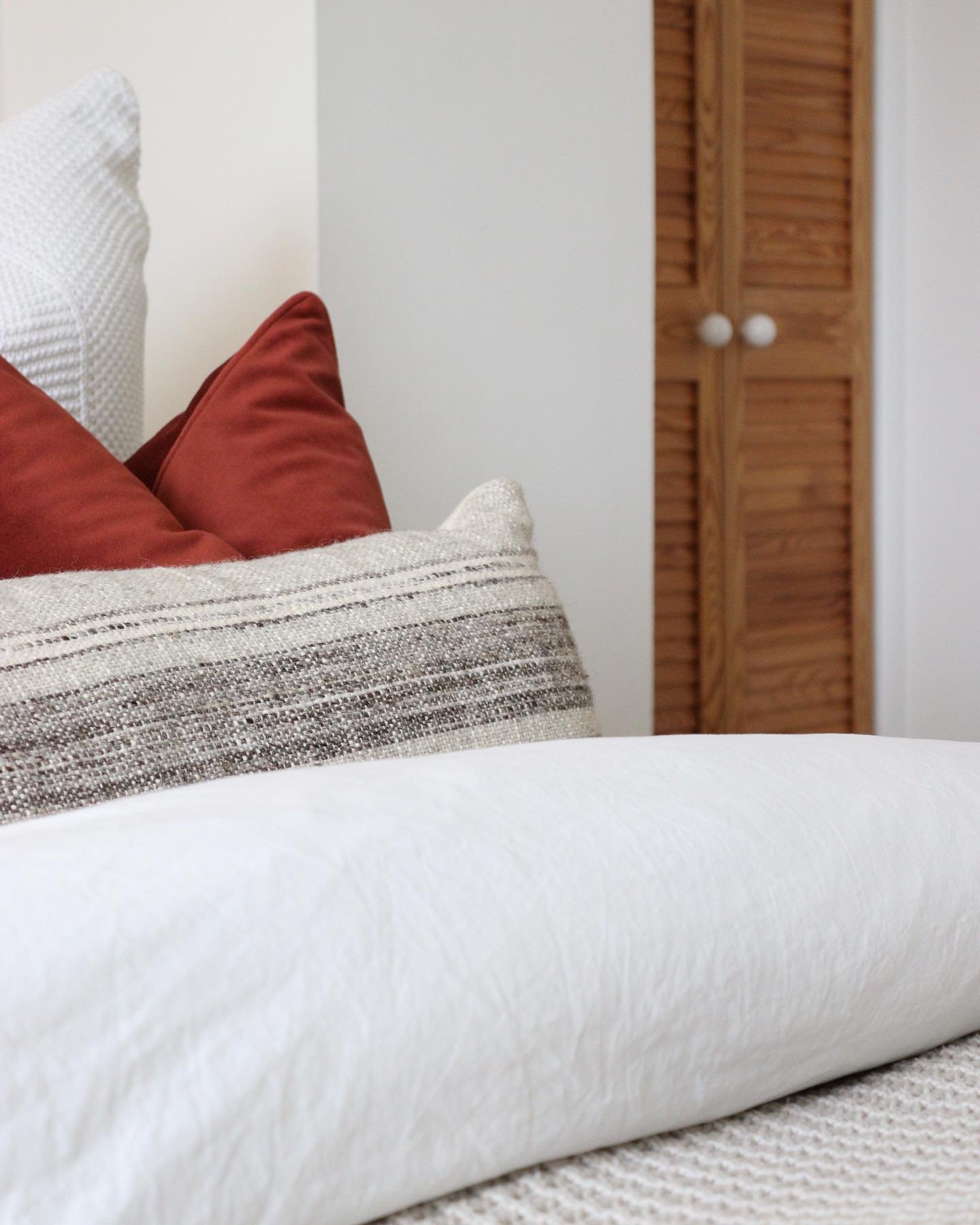 Close-up of various decorative pillows on a bed, with a wooden closet in the background.