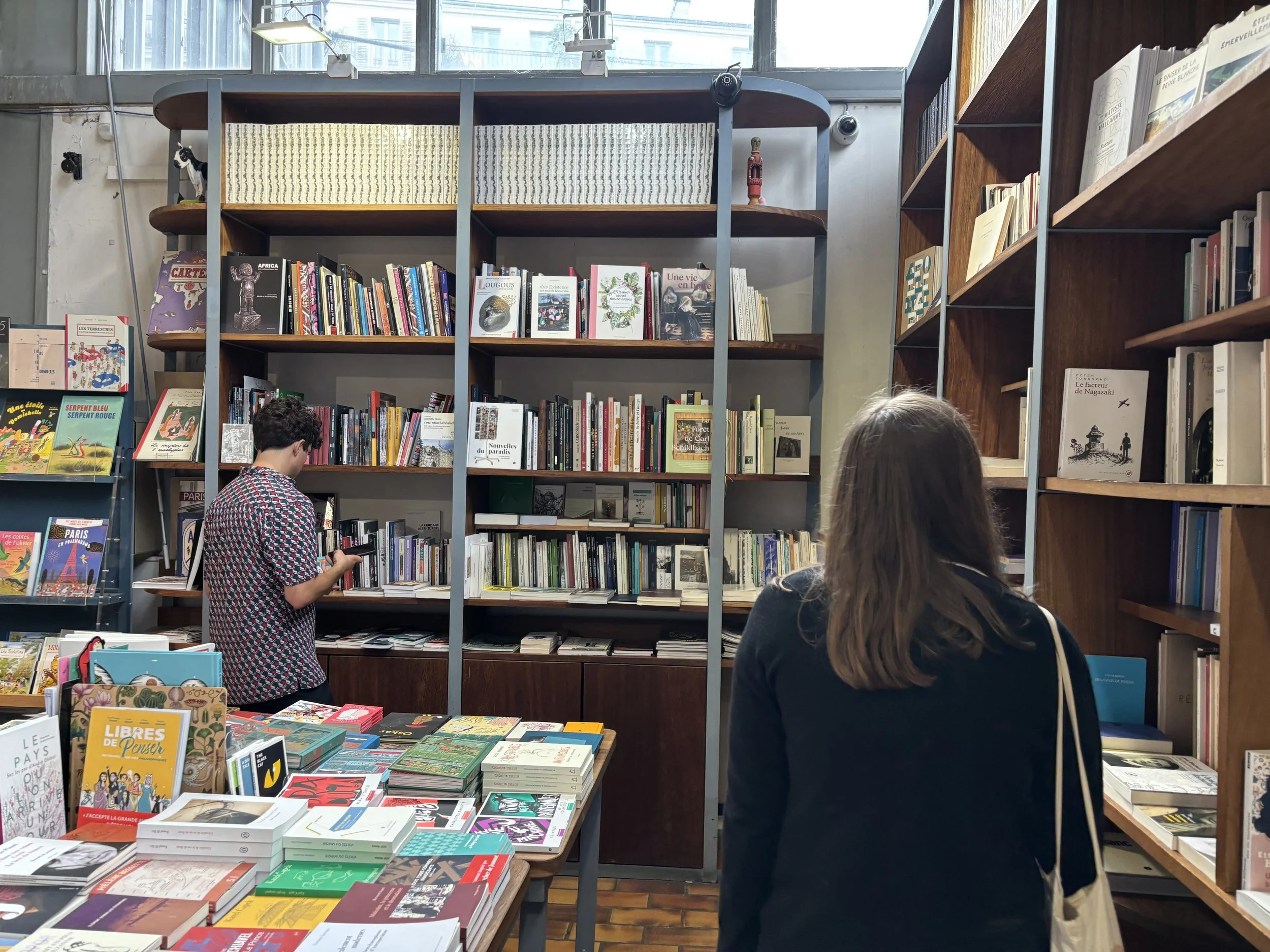 Two women in a bookstore or library browsing bookshelves, with a display table of books in the foreground.