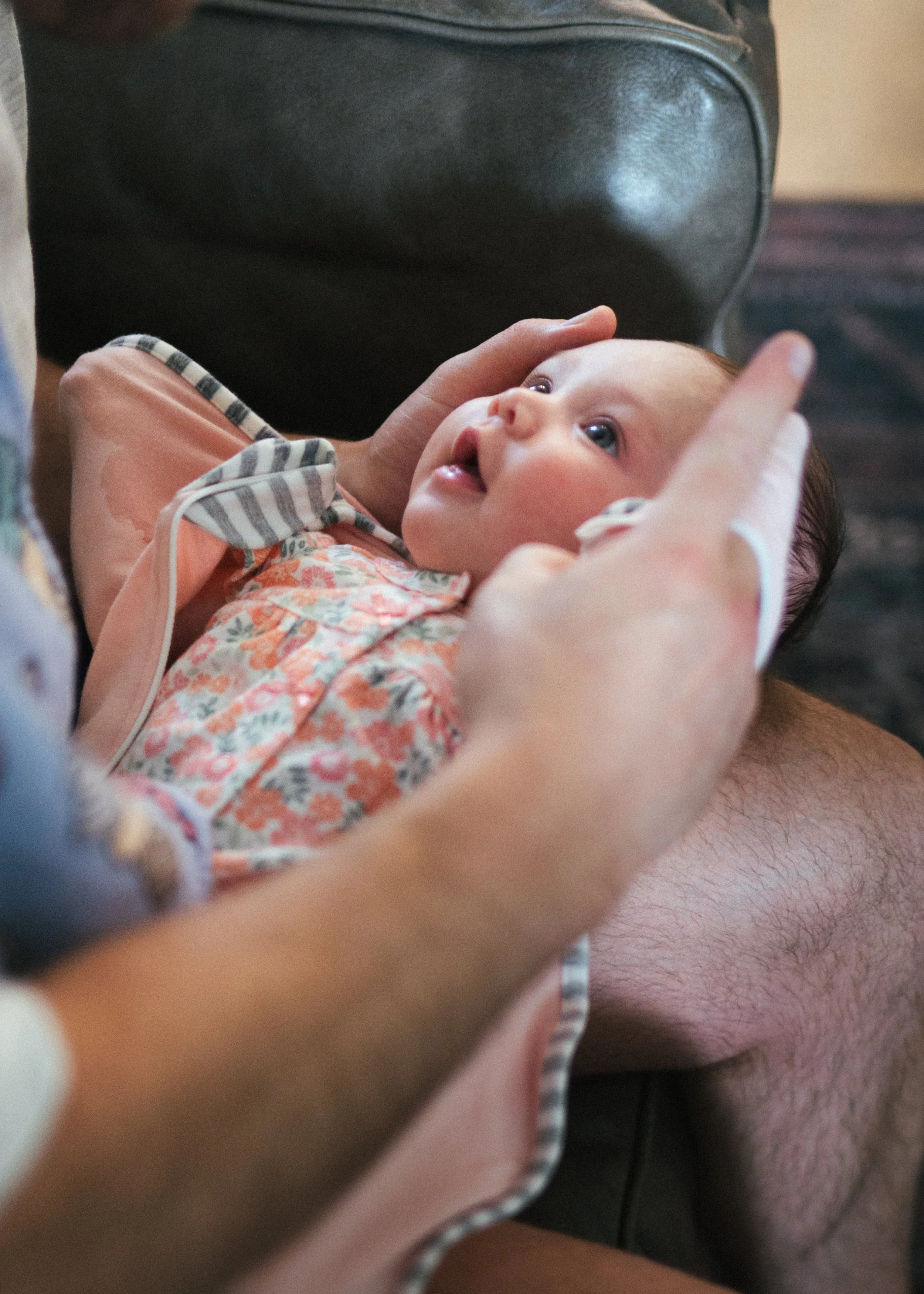 A baby lying on an adult's lap, being gently held and touched on the face, with a black leather bag in the background.