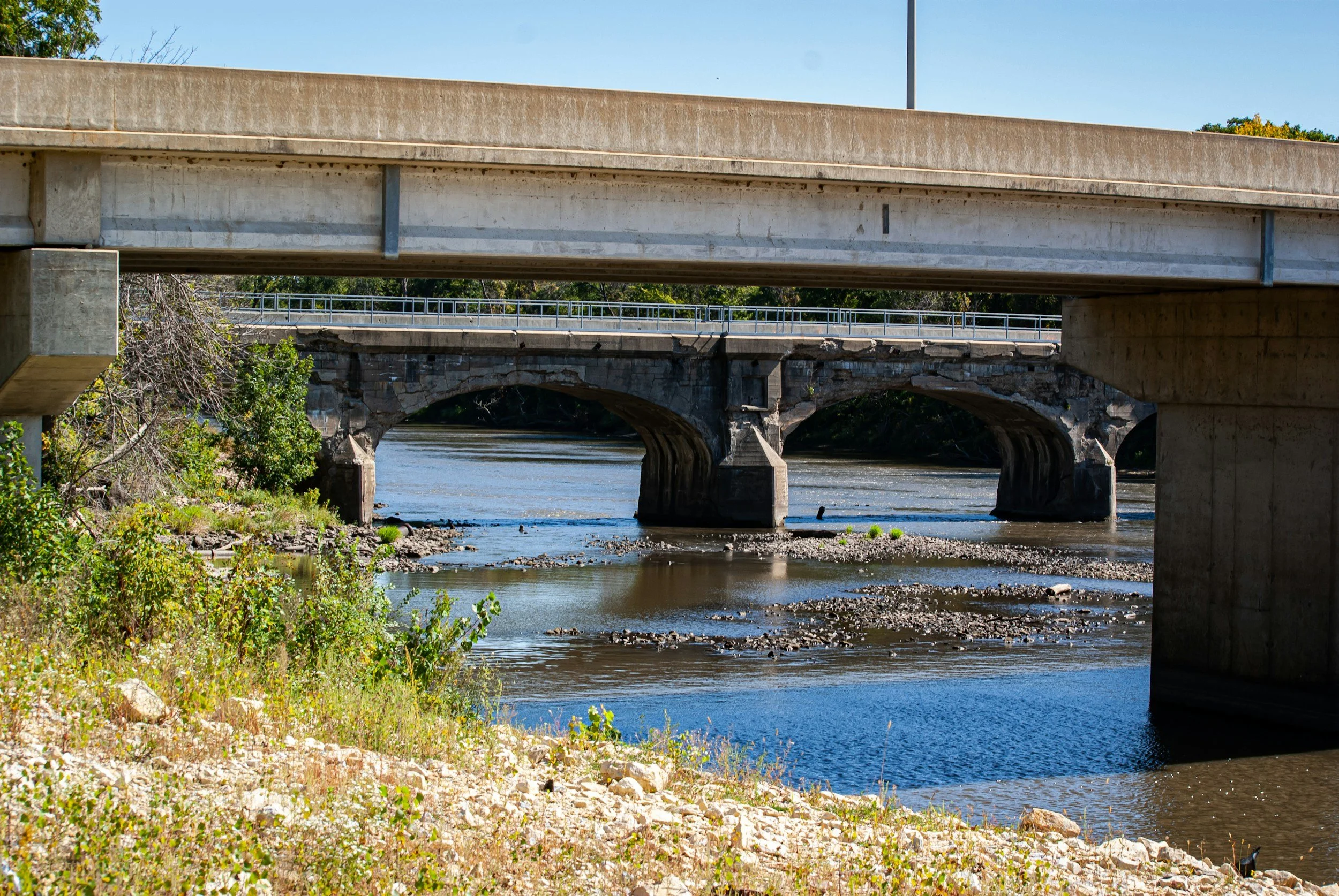 Two bridges over a river with trees and rocks at the riverbank.