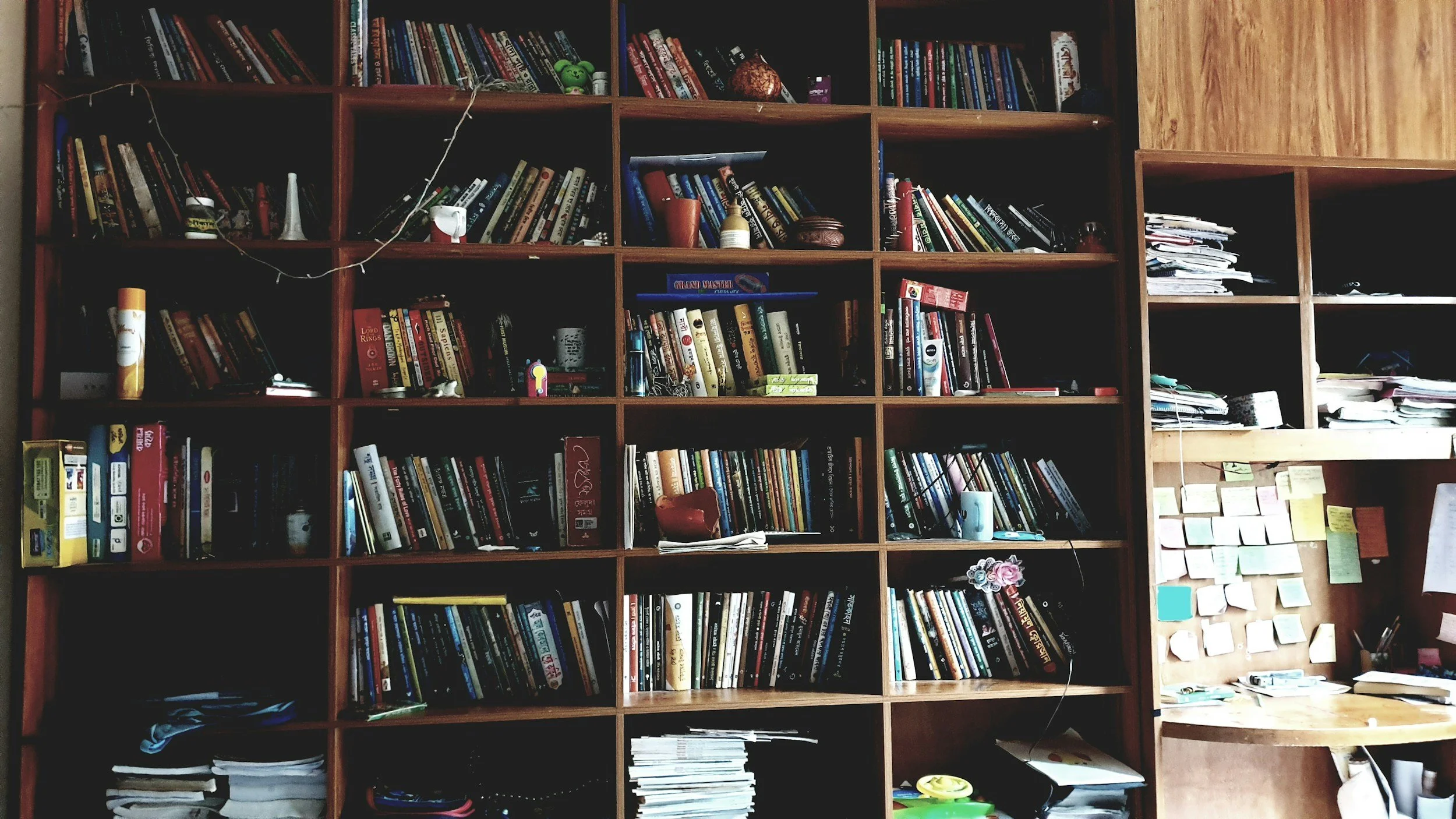 Bookshelf filled with books, papers, and small miscellaneous objects, with some items on a desk nearby.