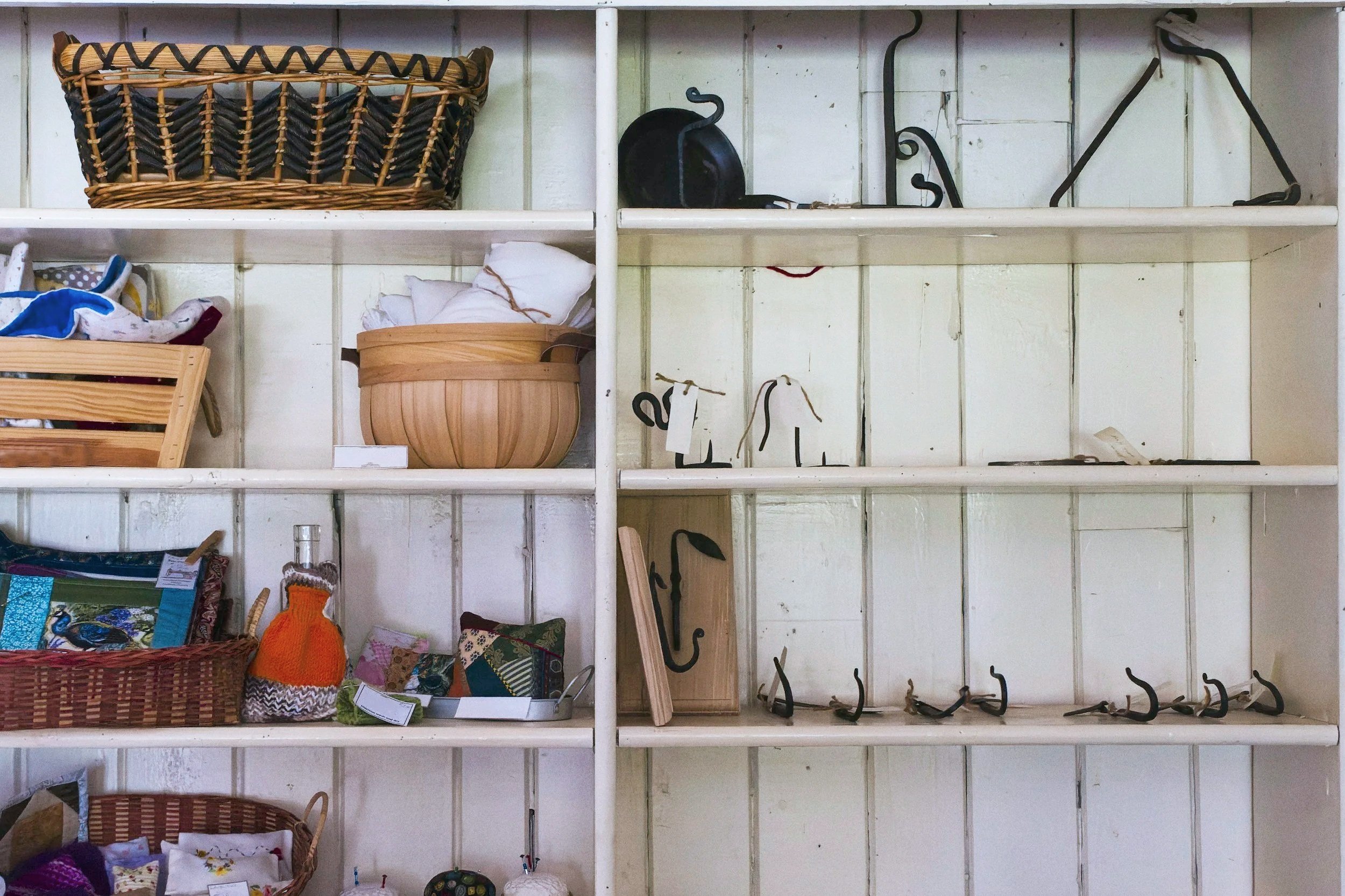 Empty white wooden shelves with hooks, baskets, and miscellaneous household items