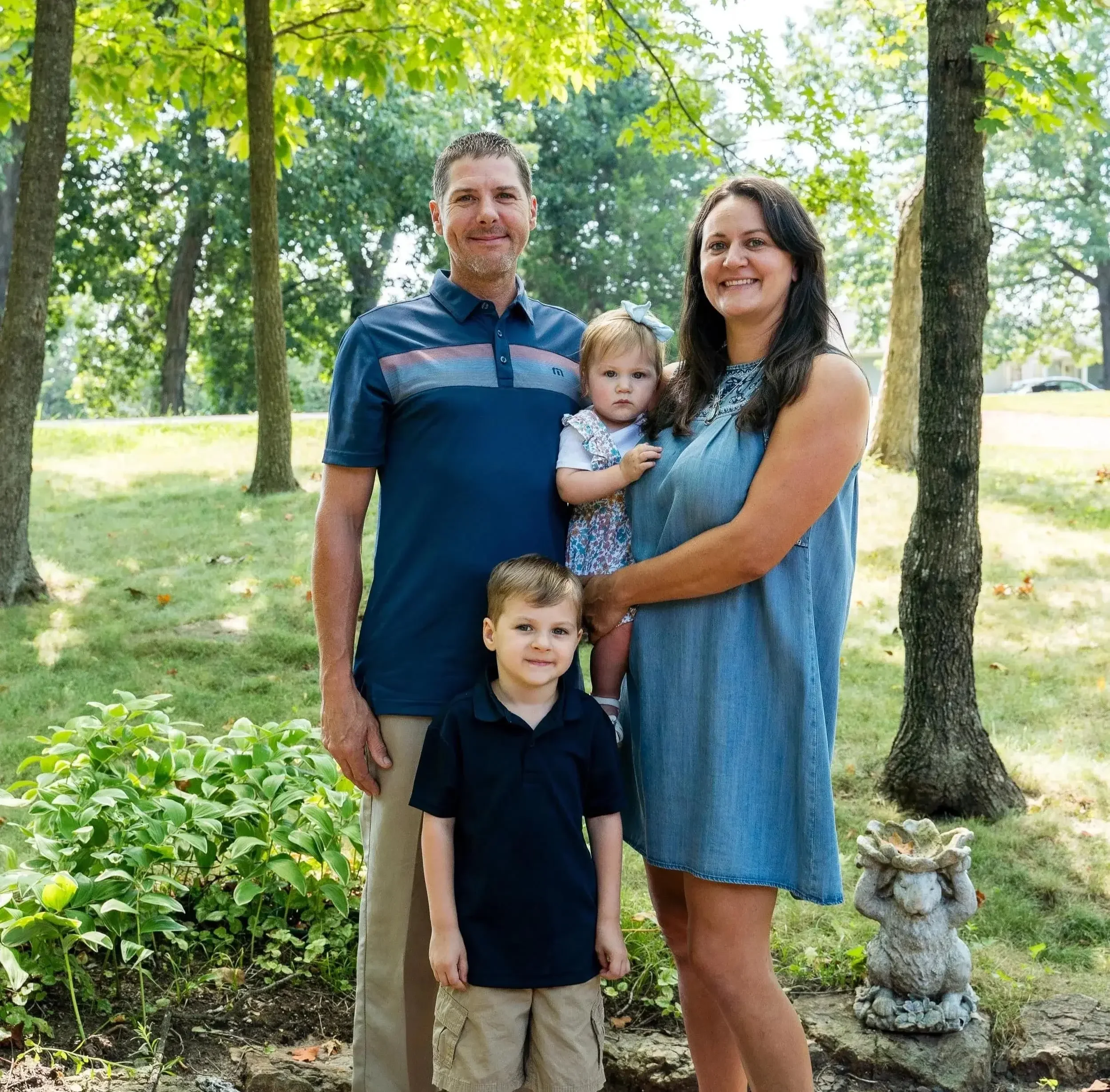 Family portrait of four standing outdoors in a park.