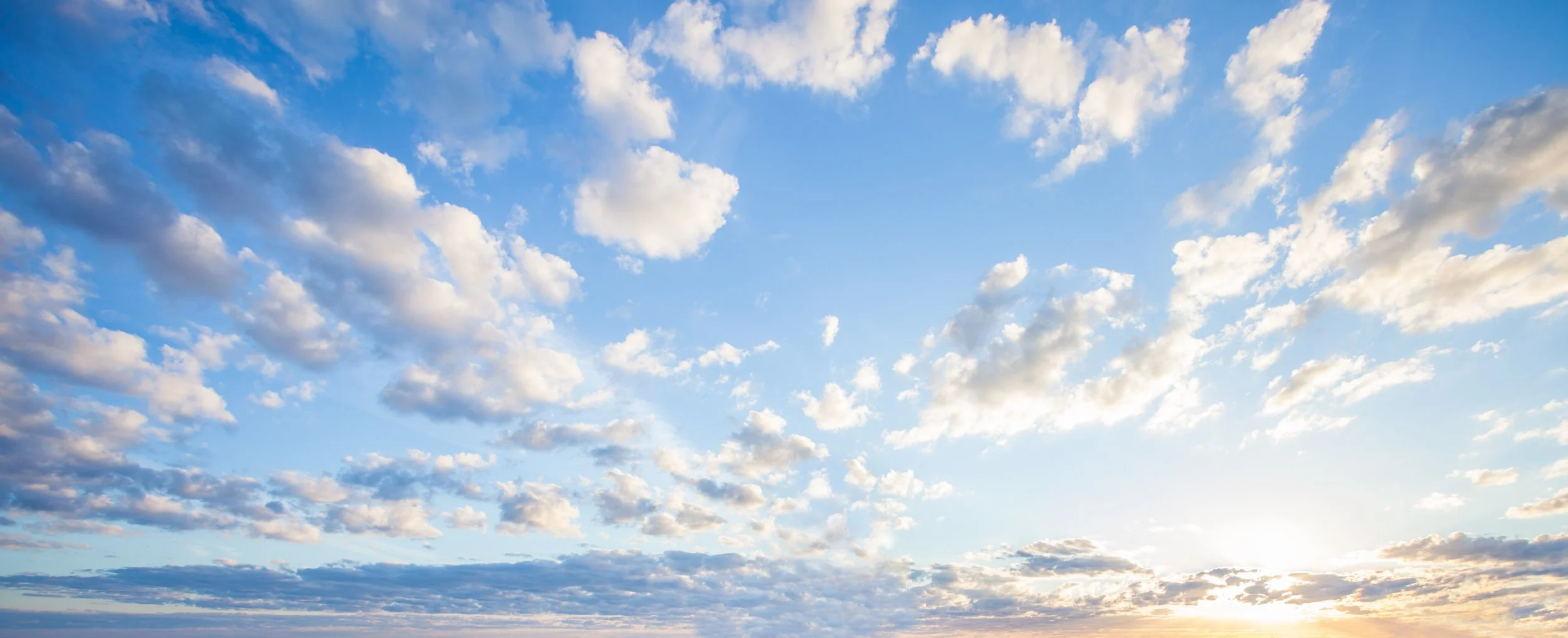 A bright sky with scattered clouds and the sun near the horizon.