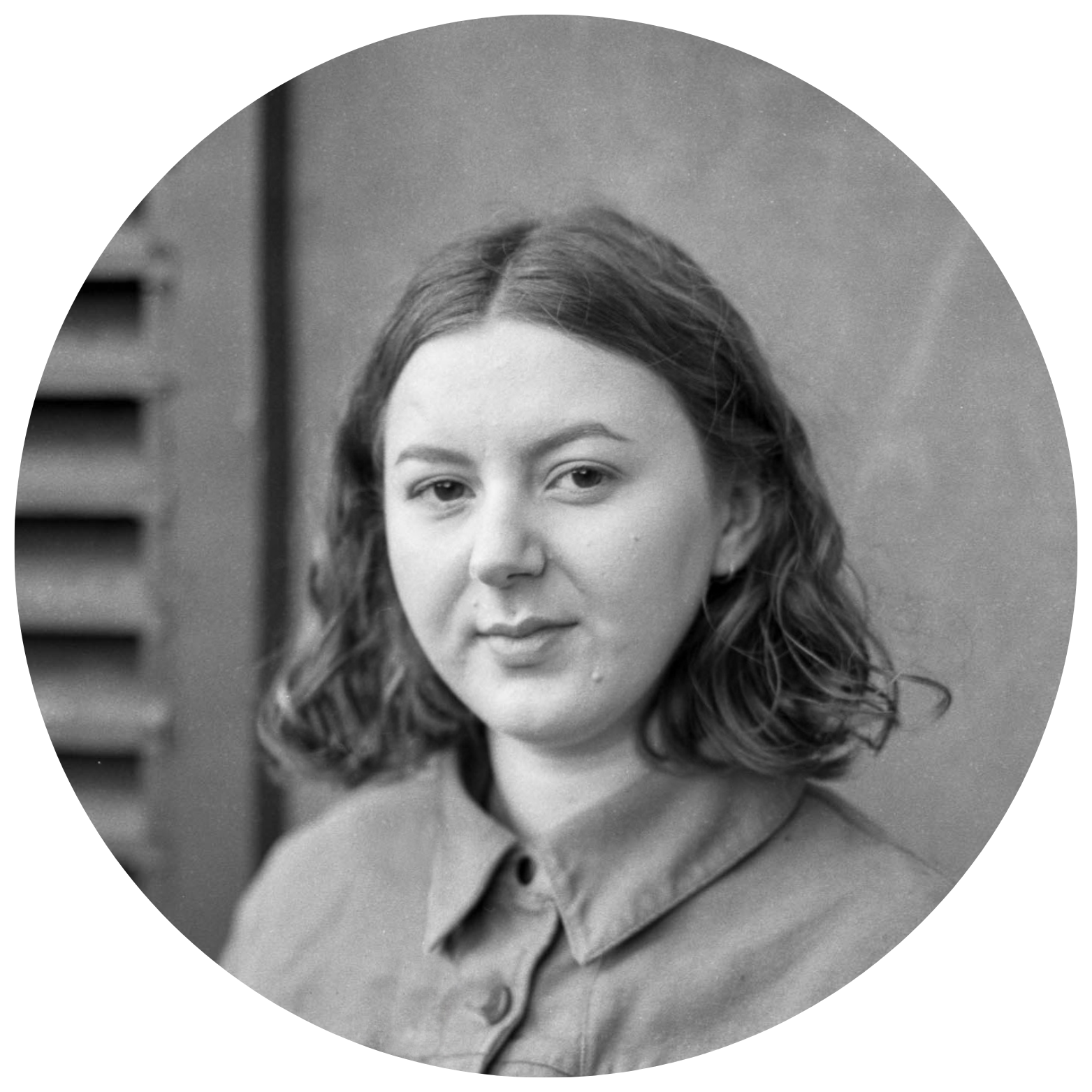 A black and white portrait of a young woman with wavy hair wearing a collared shirt, looking at the camera with a neutral expression.