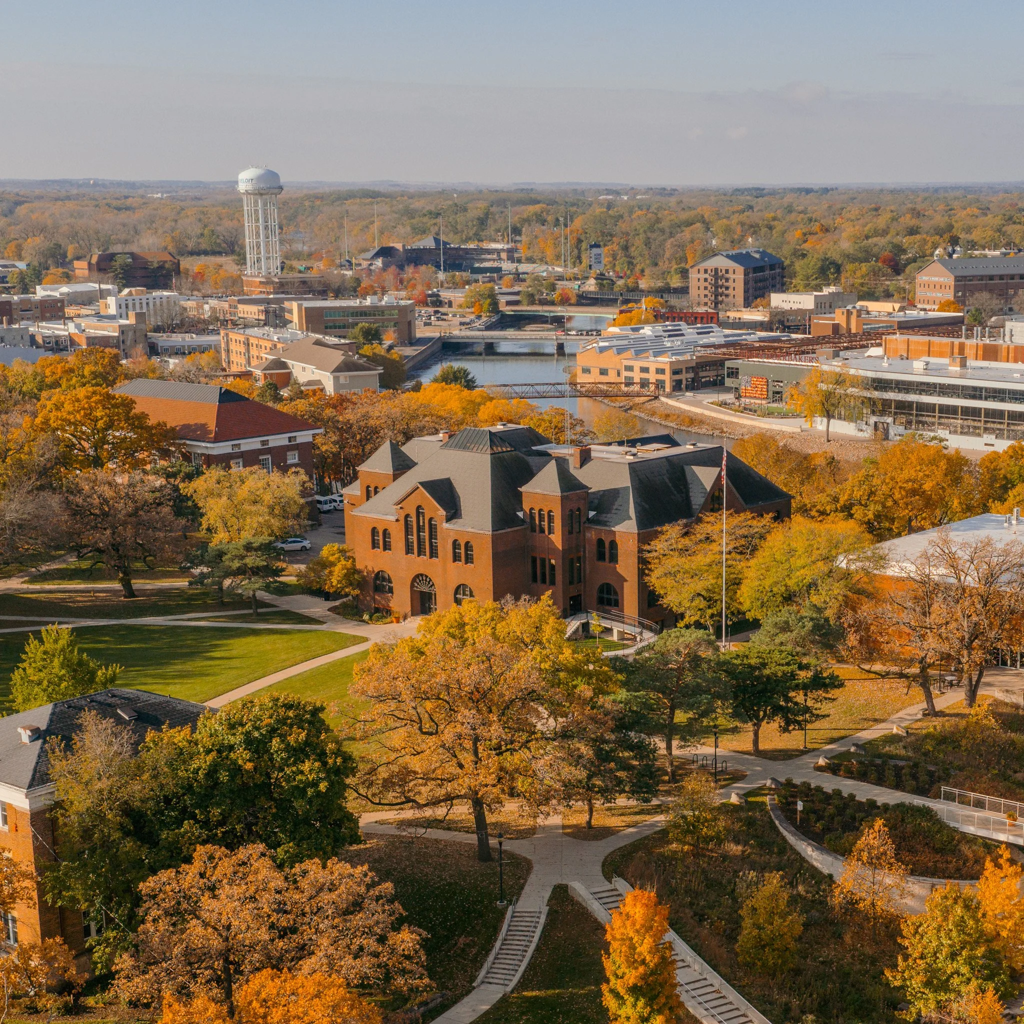 Aerial view of a city with autumn trees, a water tower, bridges crossing a river, and several commercial and residential buildings.