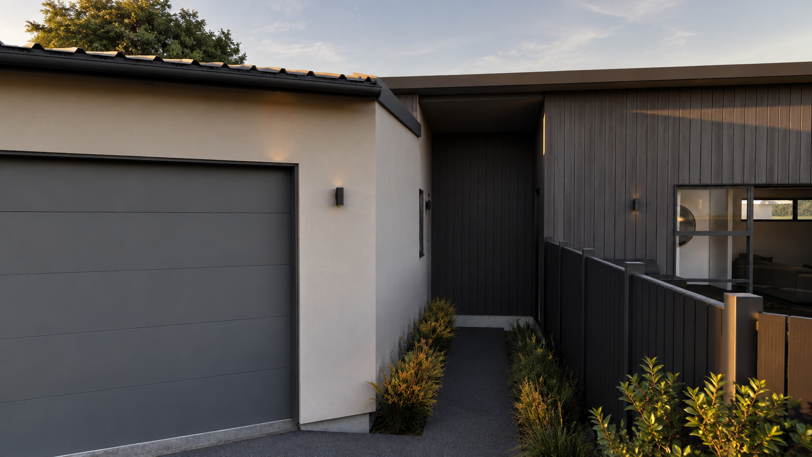 Modern house with a gray garage door, white and dark wooden exterior walls, small garden along pathway, and sunset lighting.