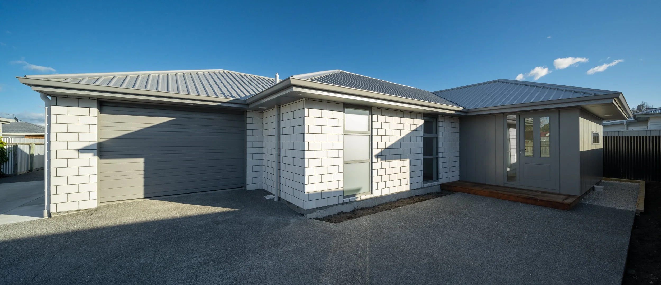 Modern house with white brick walls, metal roof, garage, and a small porch under clear blue sky  in Blenheim New Zealand