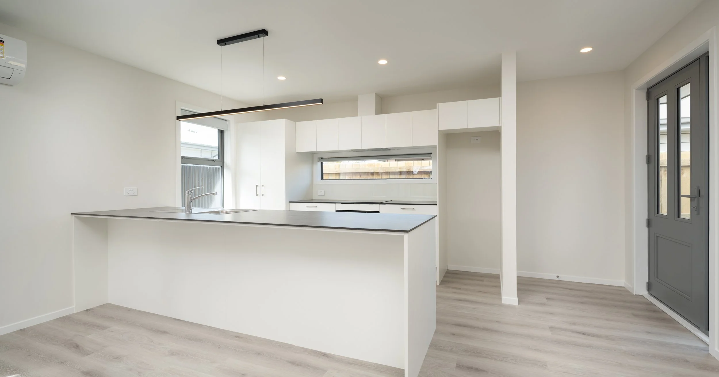 Modern kitchen with white cabinets, black countertops, and a kitchen island with a sink, large windows, and a gray door in Blenheim New Zealand