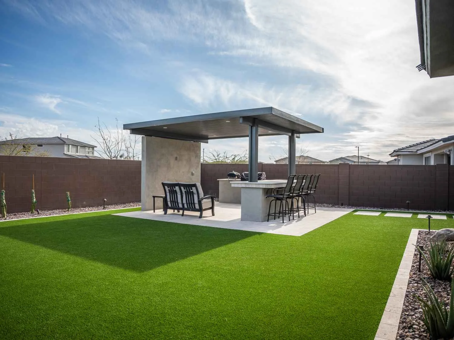 A covered outdoor kitchen with a modern pergola in Paradise Valley, AZ surrounded by artificial turf