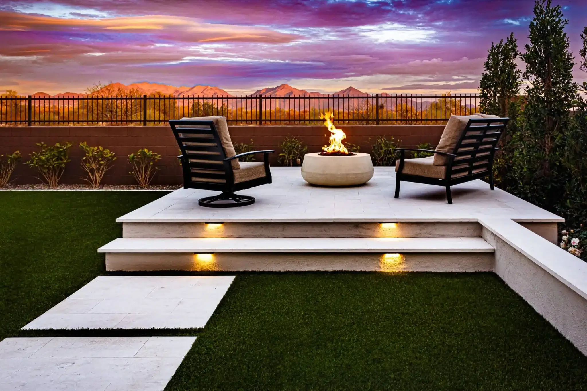 A modern outdoor patio with two chairs and a firepit, overlooking mountains at sunset in Surprise, AZ