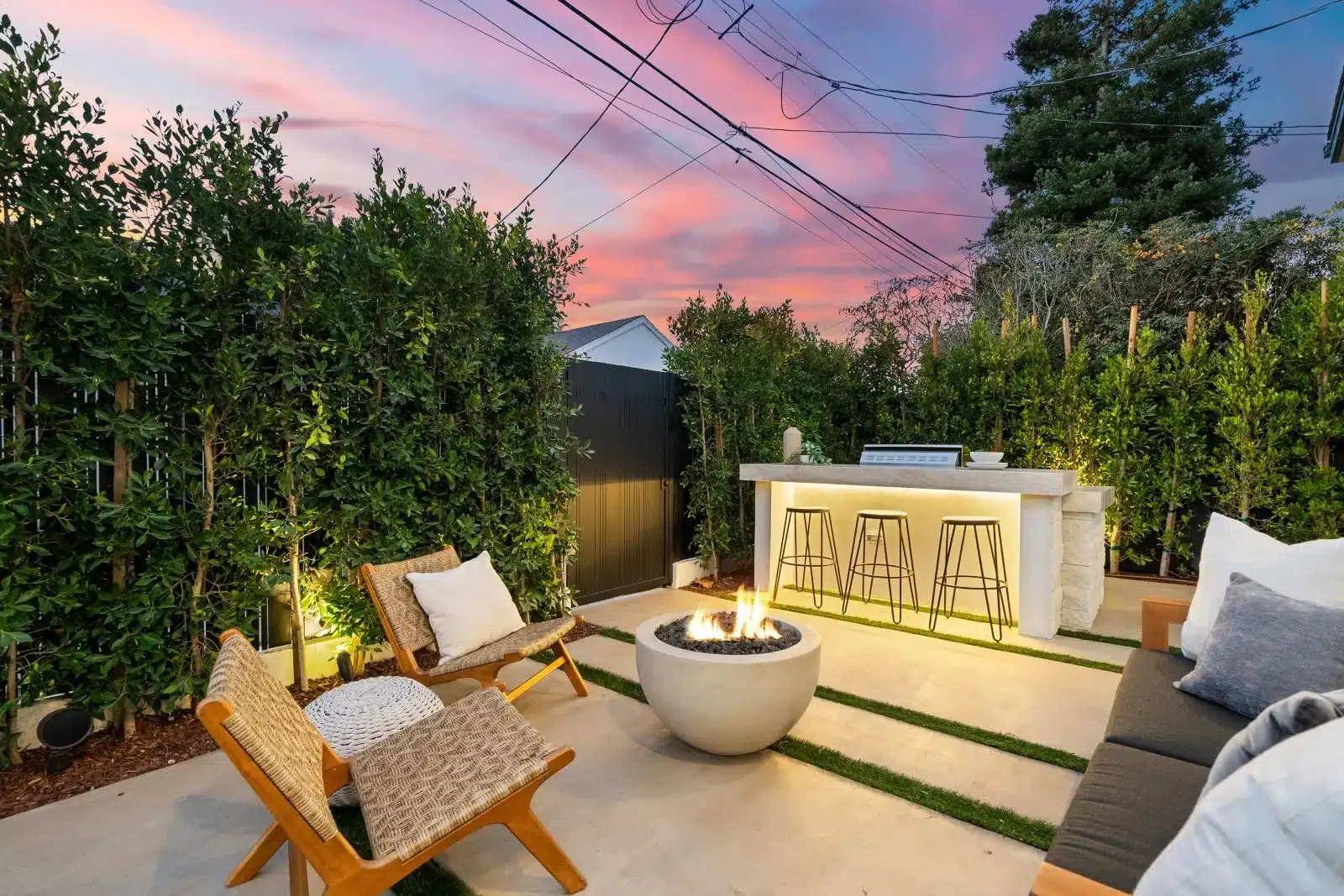 Outdoor patio with fire pit, lounge chairs, bar area, and surrounded by greenery under a pink and purple sunset sky in Vistancia, AZ