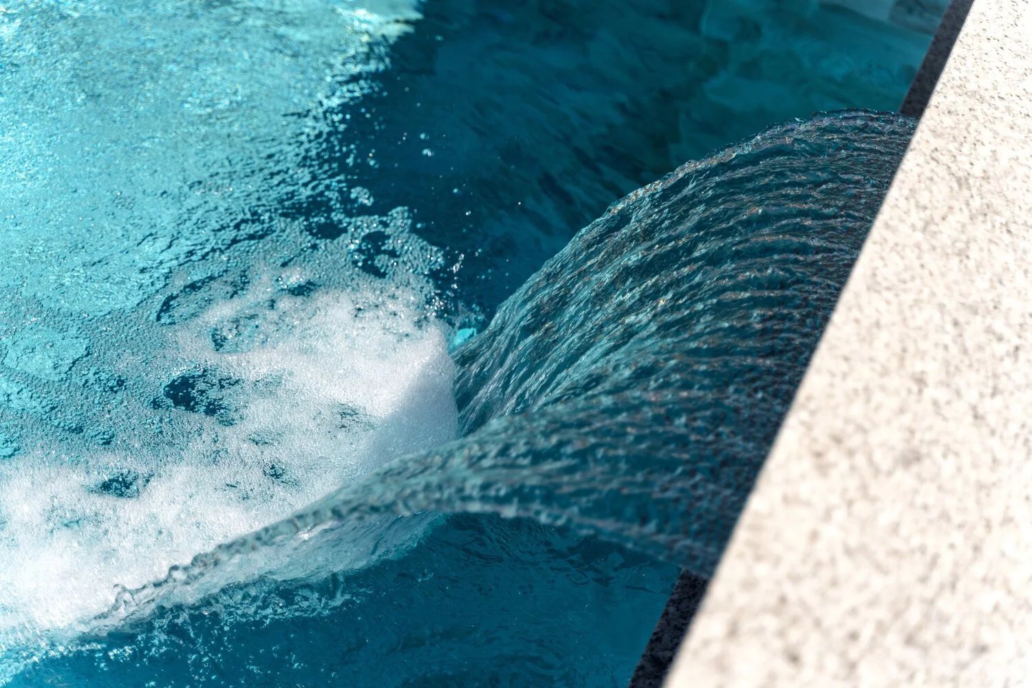 Close-up of a waterfall or water feature flowing over a curved surface with bubbling water and a textured stone or concrete edge in Scottsdale, AZ