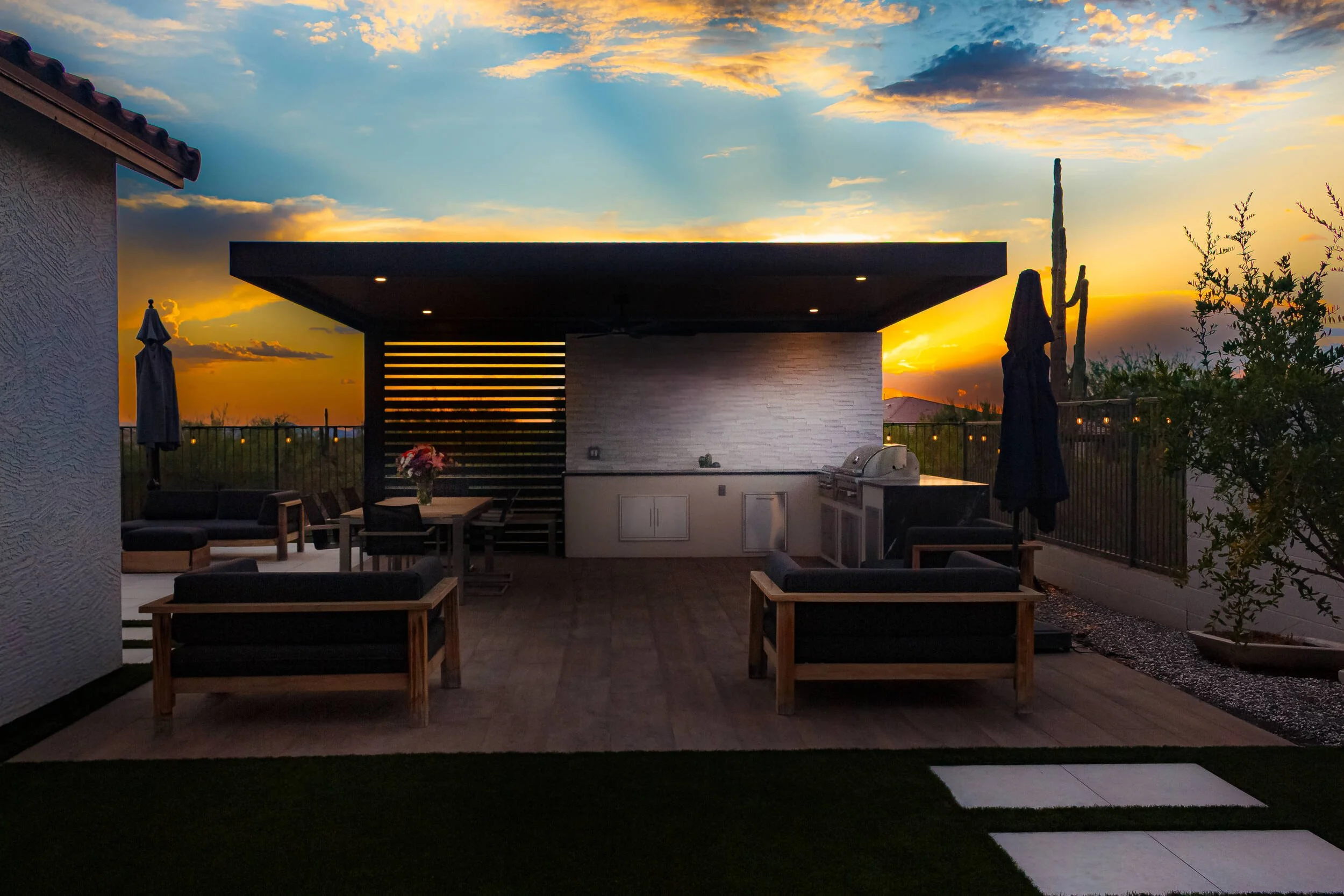 Outdoor patio area during sunset with a built-in kitchen, dining table with flowers, seating area, and umbrellas in Chandler, AZ