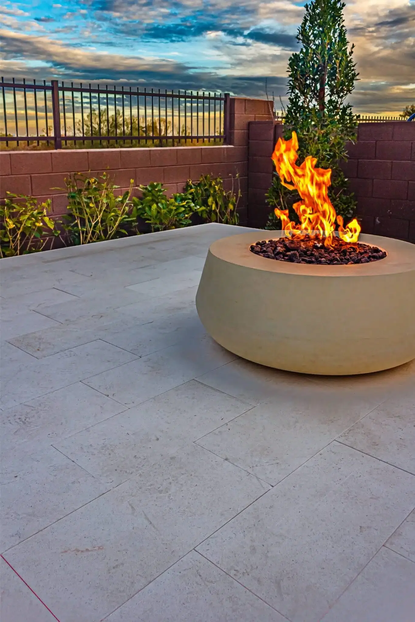 Outdoor patio with a modern fire pit, plants along a brick wall, and a cloudy sunset sky in Arcadia, AZ