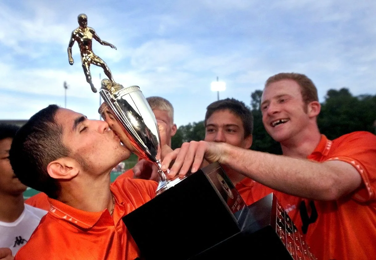 Monroe senior Erik Williams kisses the trophy held by Alex Pagon (right) after beating Mercer Island to become the 3A State Champions.