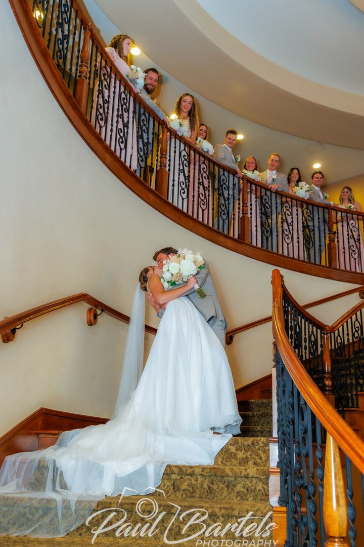 Bride and groom kissing on the stairwell with the bridal party watching