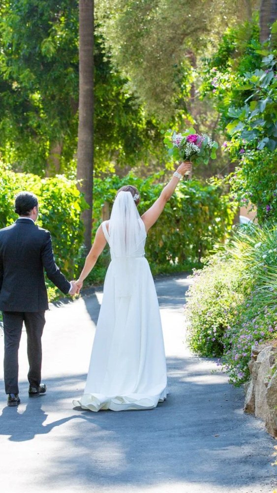 A bride and groom walking down the sidewalk with bride holding her flowers up in the air at Cottage Creek Temecula, California