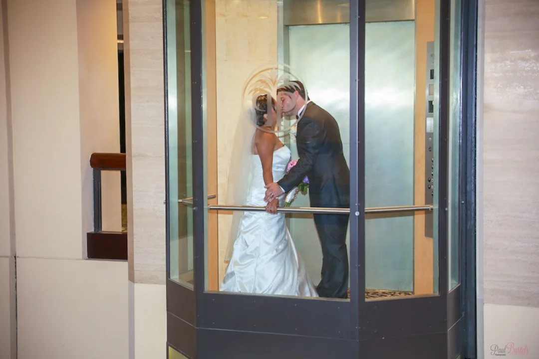 A bride and groom, kissing in an elevator after their ceremony