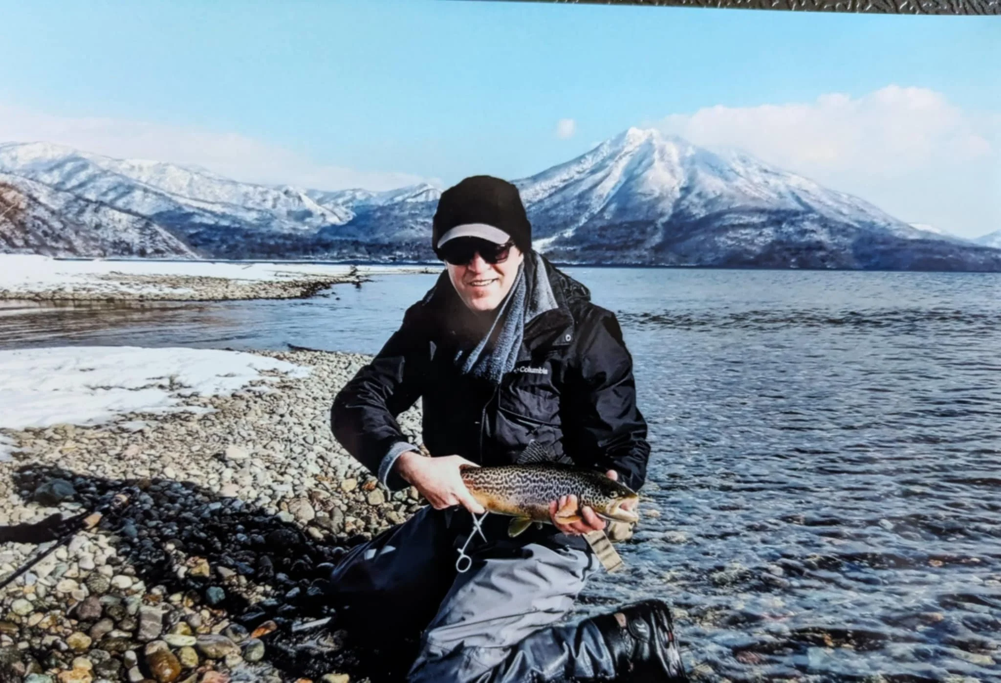 A large brown trout being held with Mt. Eniwa and Lake Shikotsu in the background