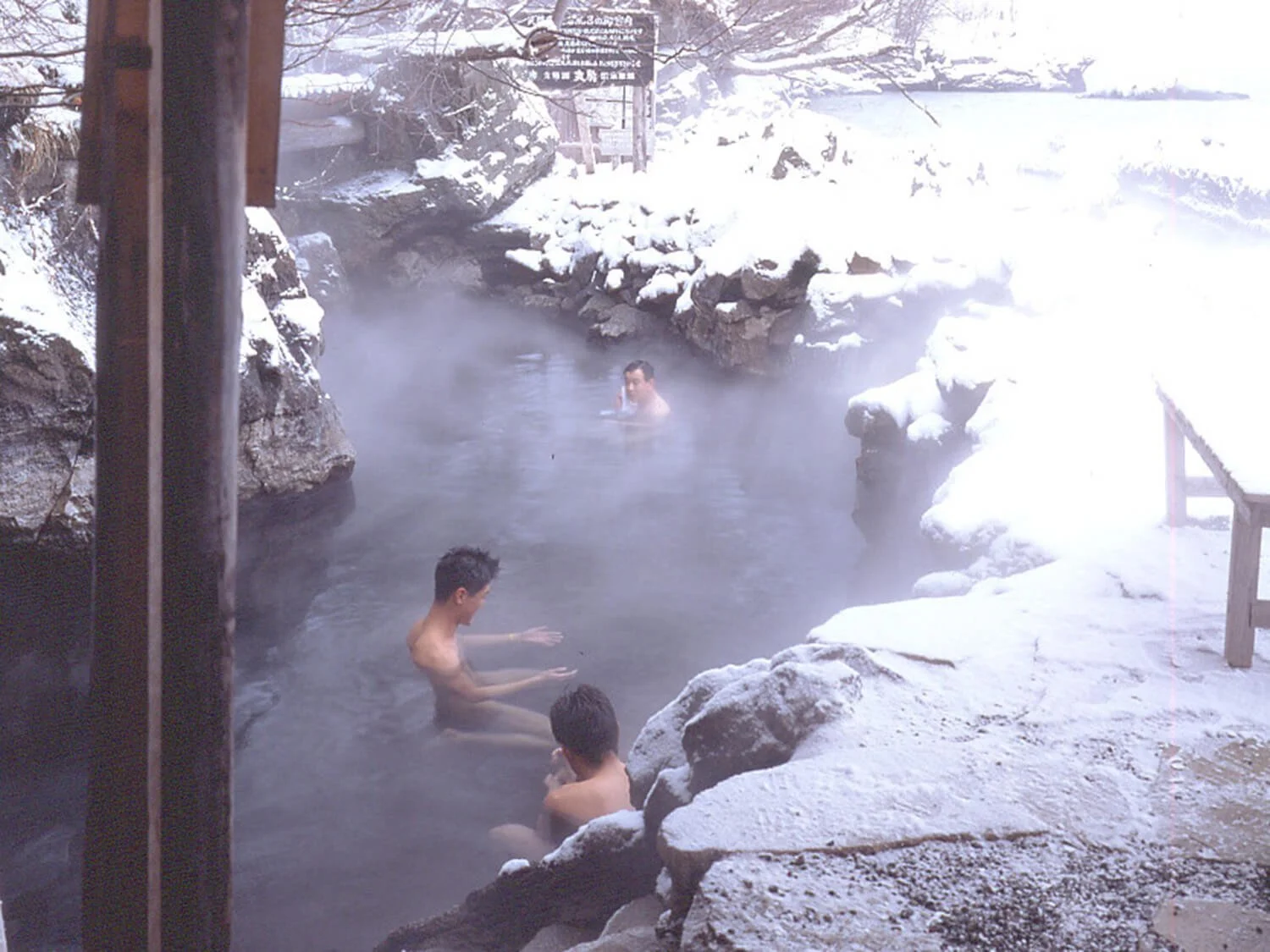 People enjoying hot spring bath outdoors in snowy winter landscape.