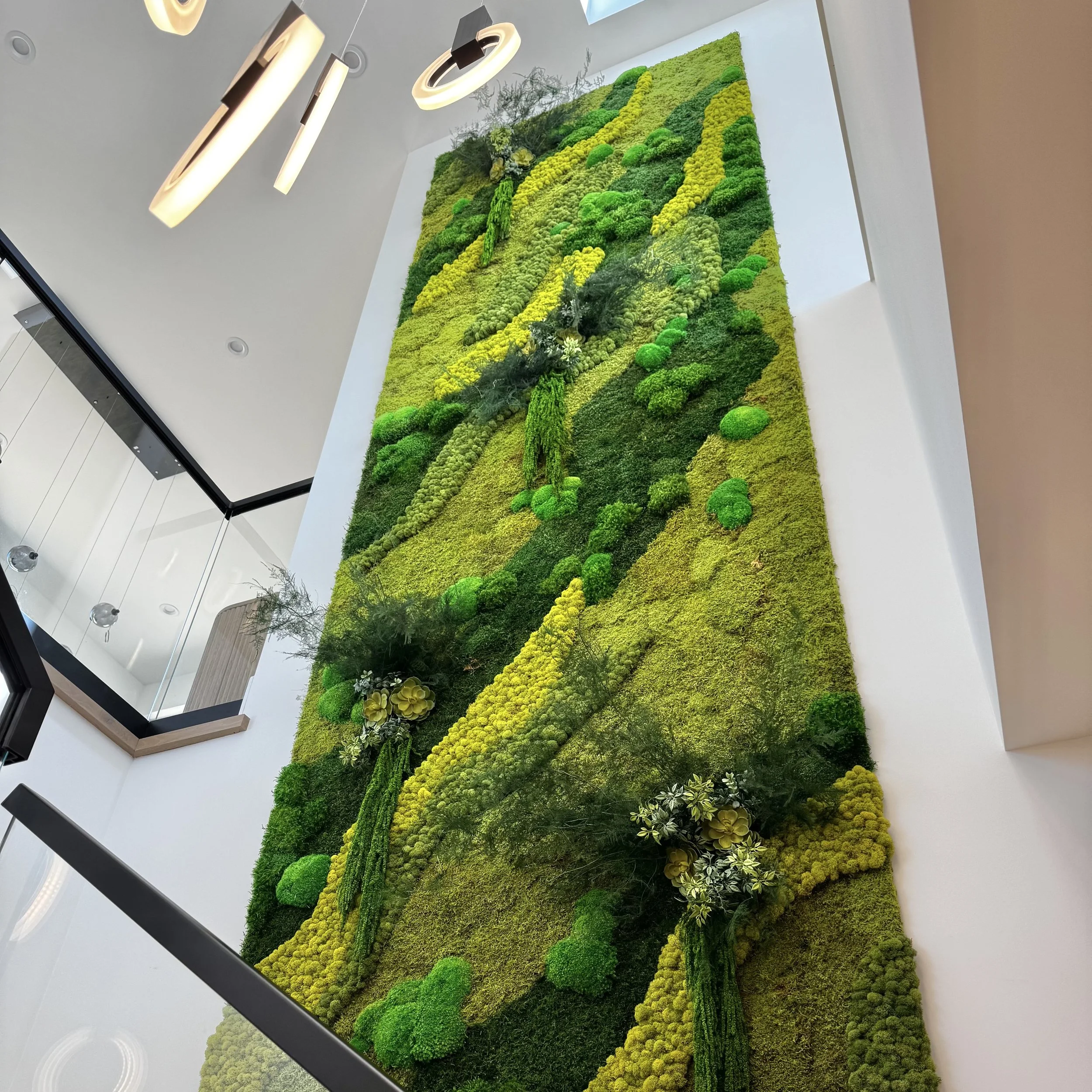 Tall moss wall in private residence using preserved reindeer moss, sheet moss, pole moss, faux succulents, and preserved foliage.