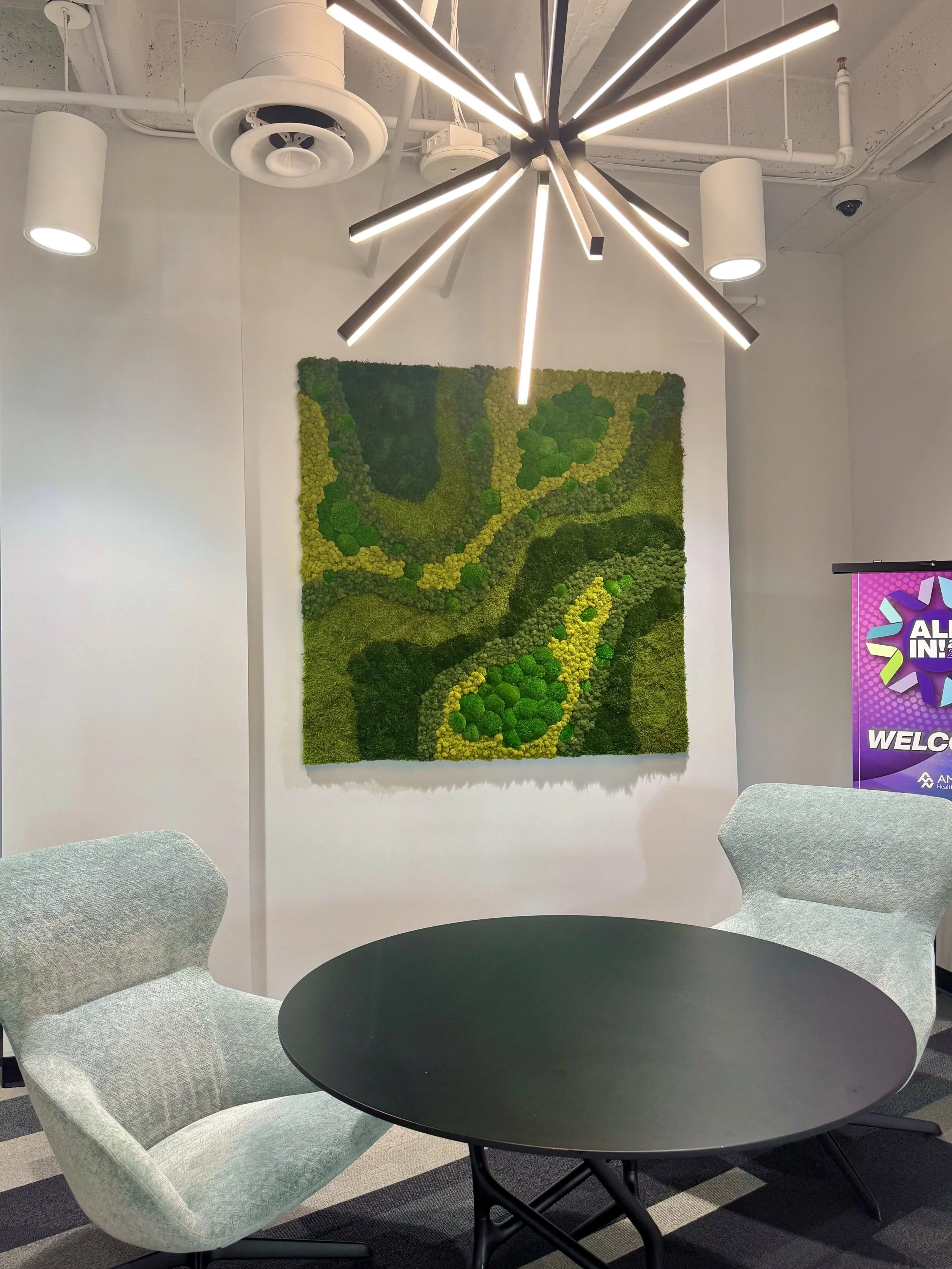 A moss wall using different preserved mosses such as sheet, mood, pole and reindeer moss in a corporate office with gray chairs and a black coffee table. 