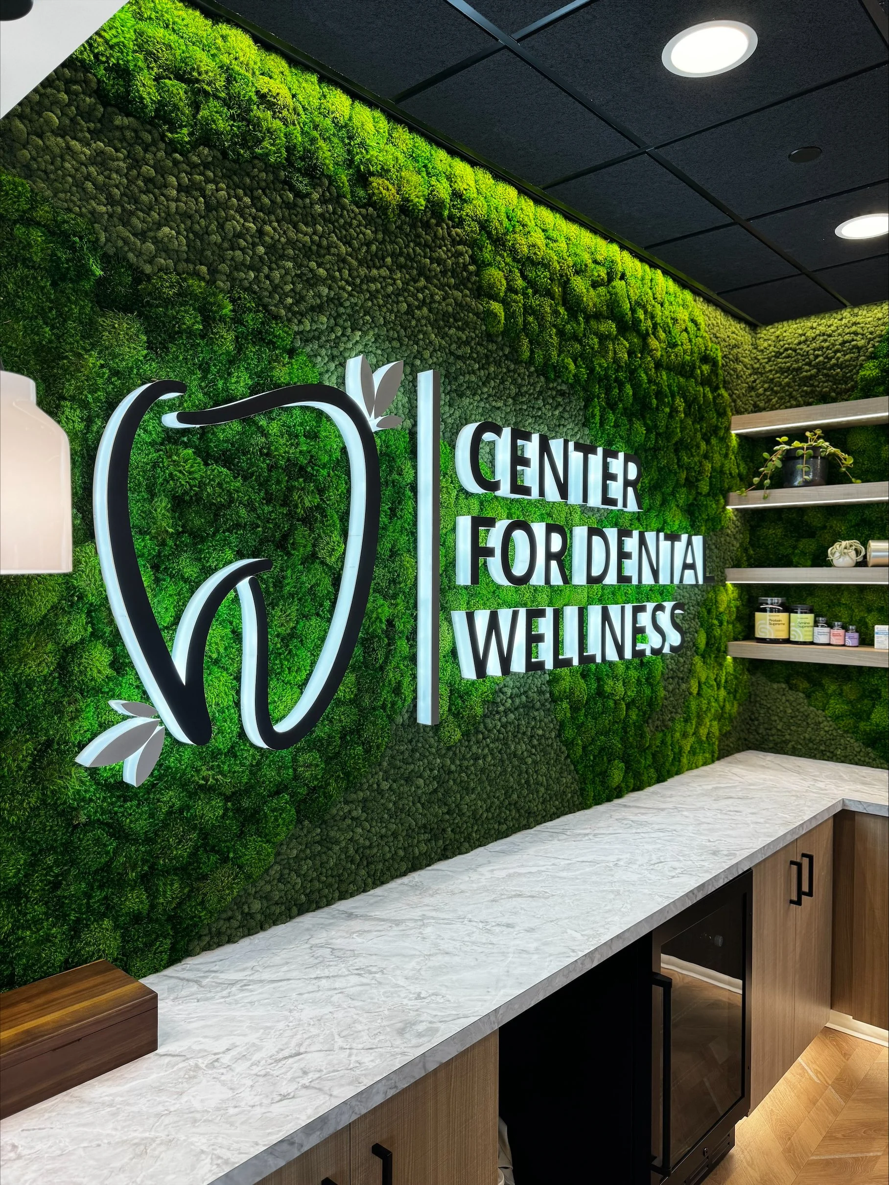 Integrated wraparound moss wall with shelves, lit sign and down lighting at a dental office in Post Falls