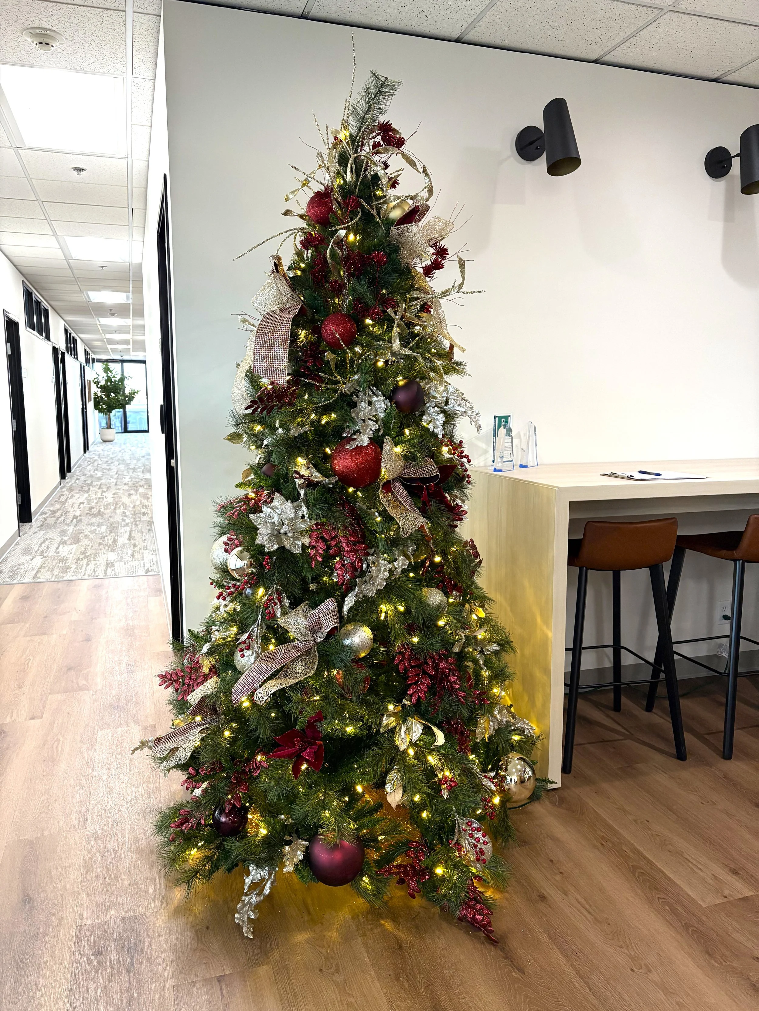 Holiday Christmas tree with red and champagne ornaments, sitting in the corner of a commercial lobby.