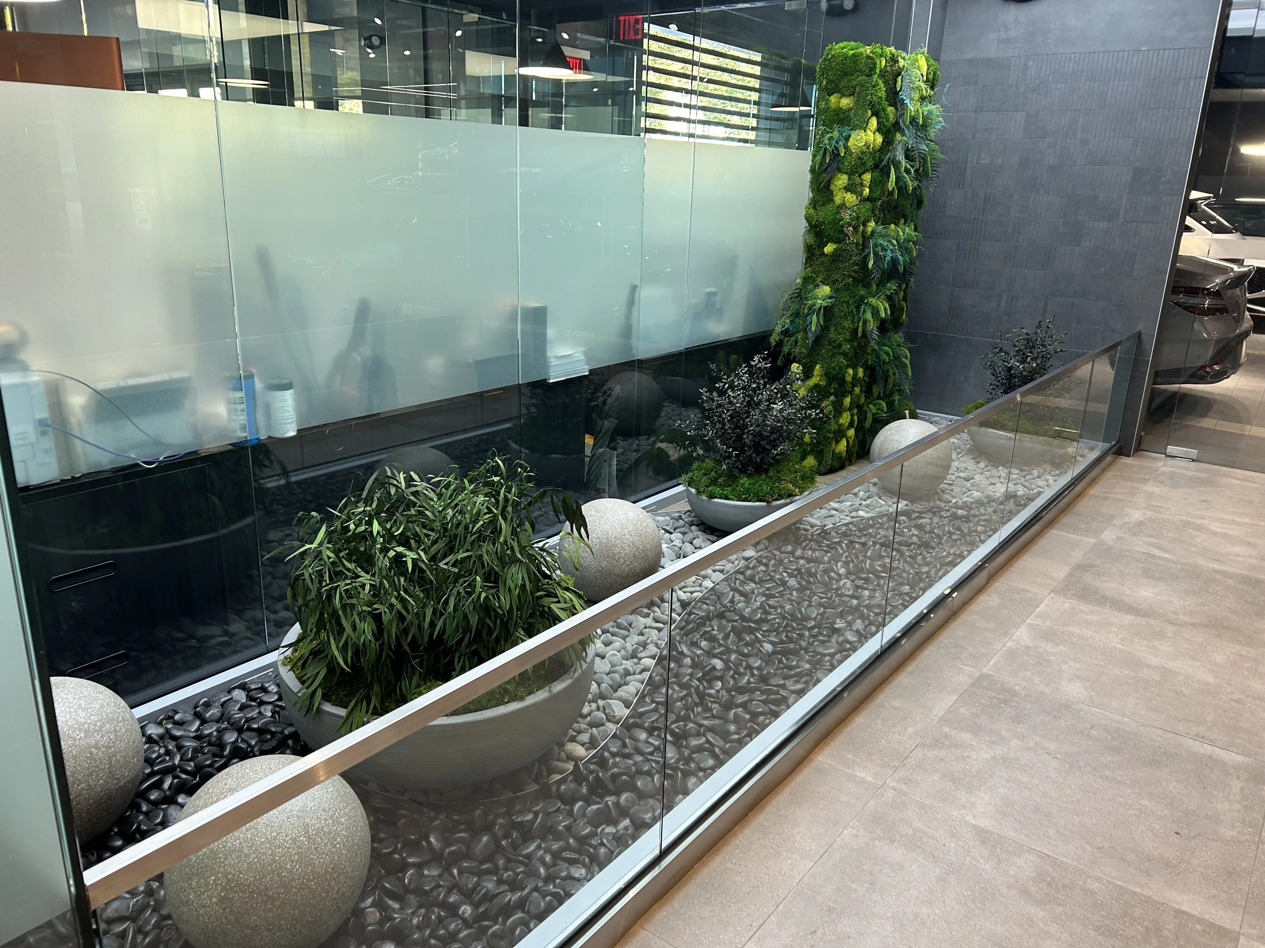 Freestanding moss wall and moss planters in a car dealership rock garden using preserved sheet moss, mood moss, pole moss and preserved foliage.