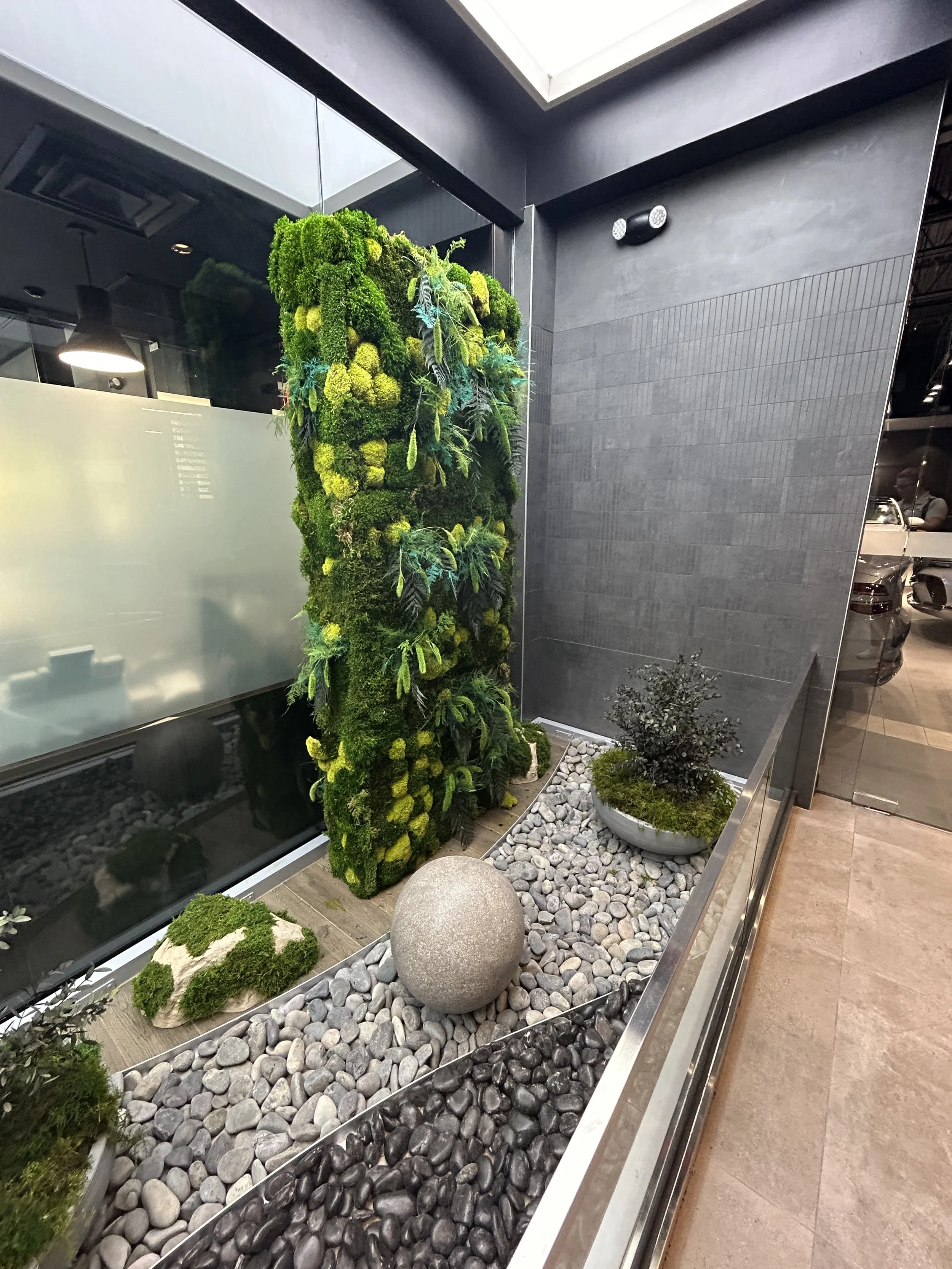 Freestanding moss wall and moss planters in a car dealership rock garden using preserved sheet moss, mood moss, pole moss and preserved foliage.