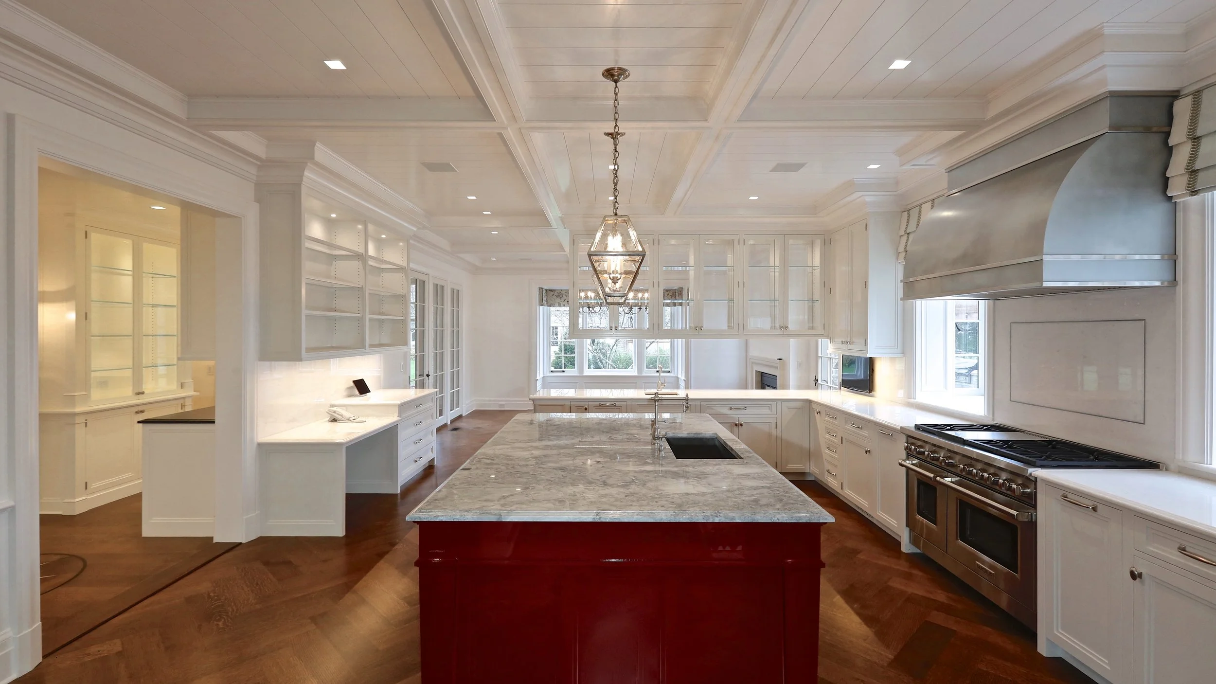 Spacious kitchen with white cabinets, a central island with a marble countertop, stainless steel appliances, and hardwood flooring.