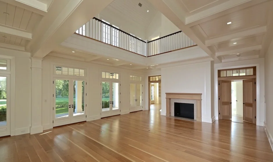 Spacious living room with white walls, wooden flooring, large windows, a fireplace, and an open second-floor balcony with white railing. Amagansett construction