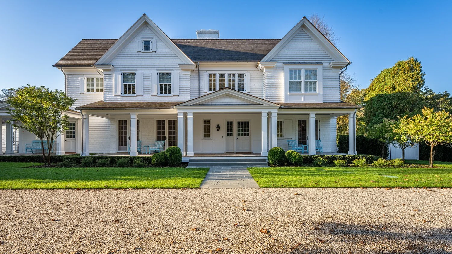 Front view of a large white wooden house with a porch, multiple windows, and a well-maintained lawn with trees on either side.