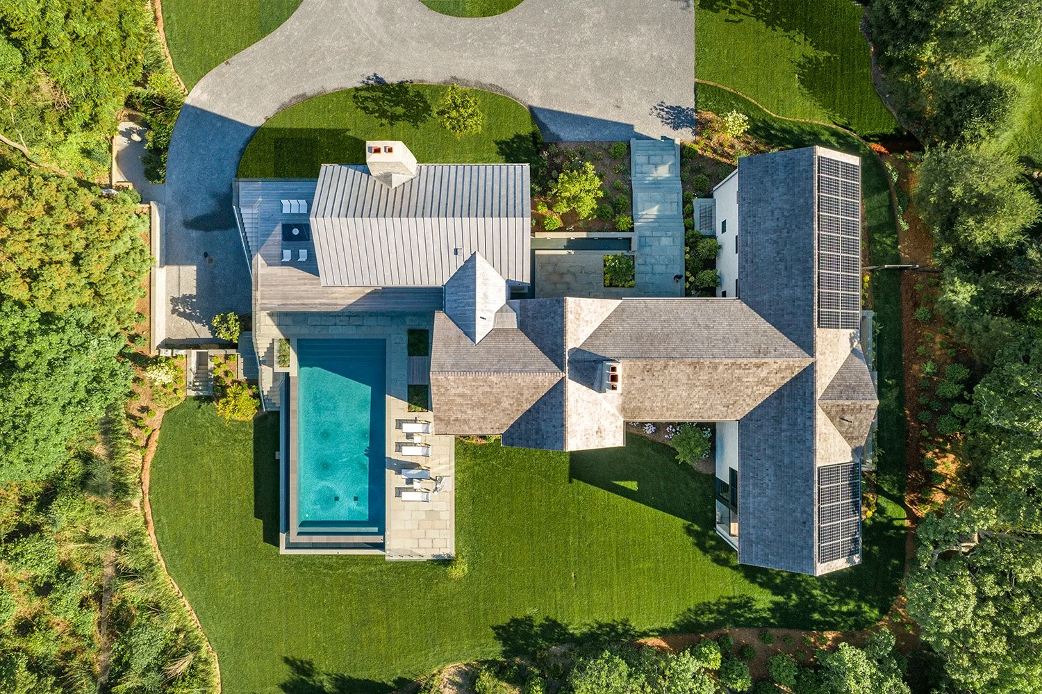 Aerial view of a large house with a swimming pool, surrounded by green grass, trees, and landscaping.