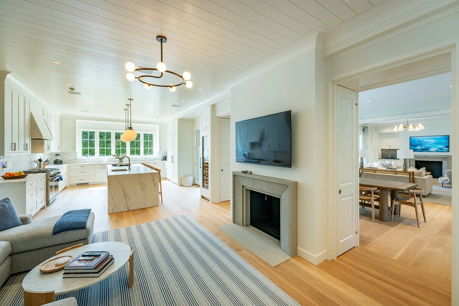 Open-concept living room and kitchen area with a fireplace, TV, and modern furnishings, bright natural light, hardwood flooring, and a view into a dining area.