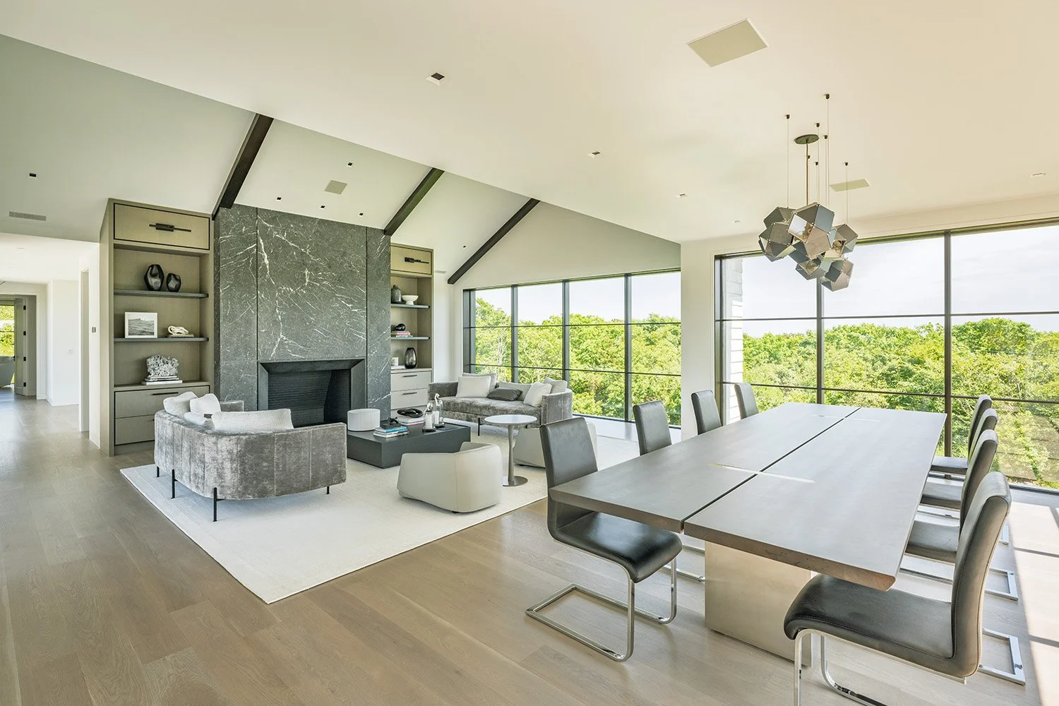 Modern living room and dining area with large windows, neutral furniture, and a unique geometric chandelier.