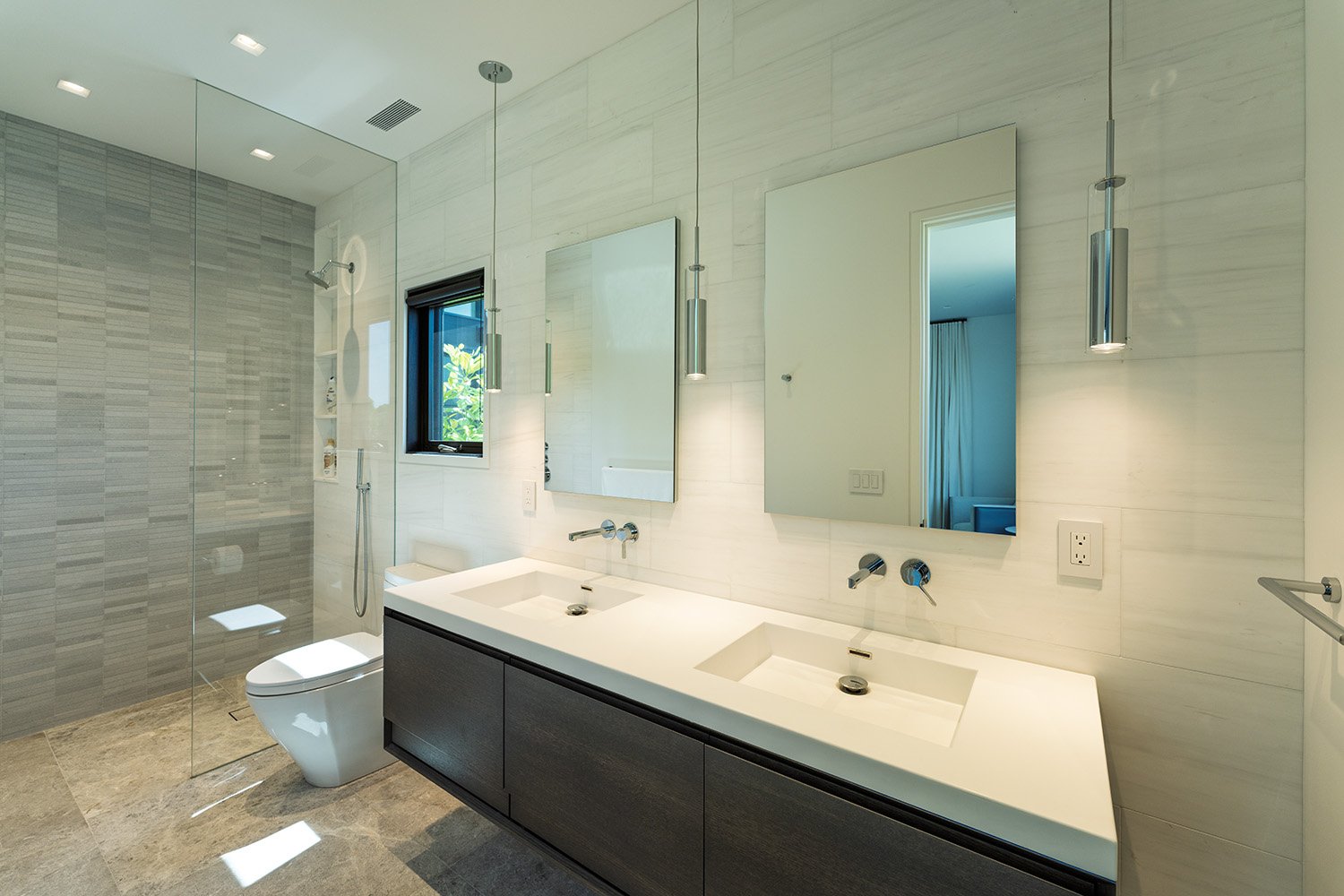 Modern bathroom with double sink vanity, large mirrors, wall-mounted faucets, and a walk-in shower with a glass partition.