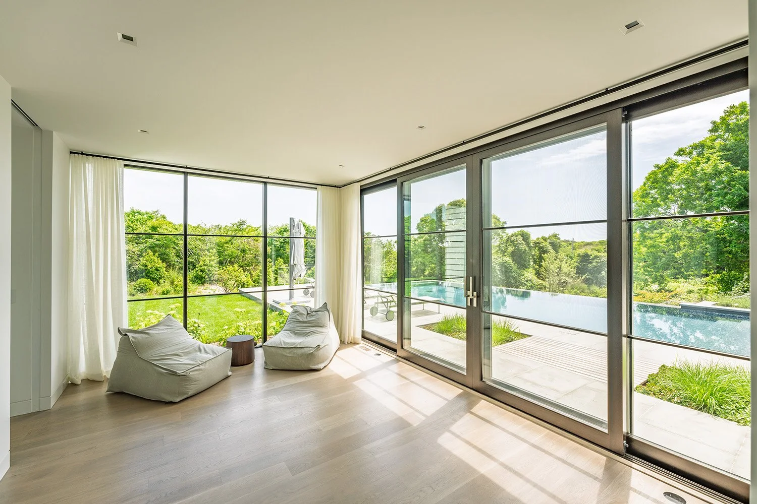 Modern living room with large glass windows overlooking a green outdoor area, with two bean bag chairs and a small side table.