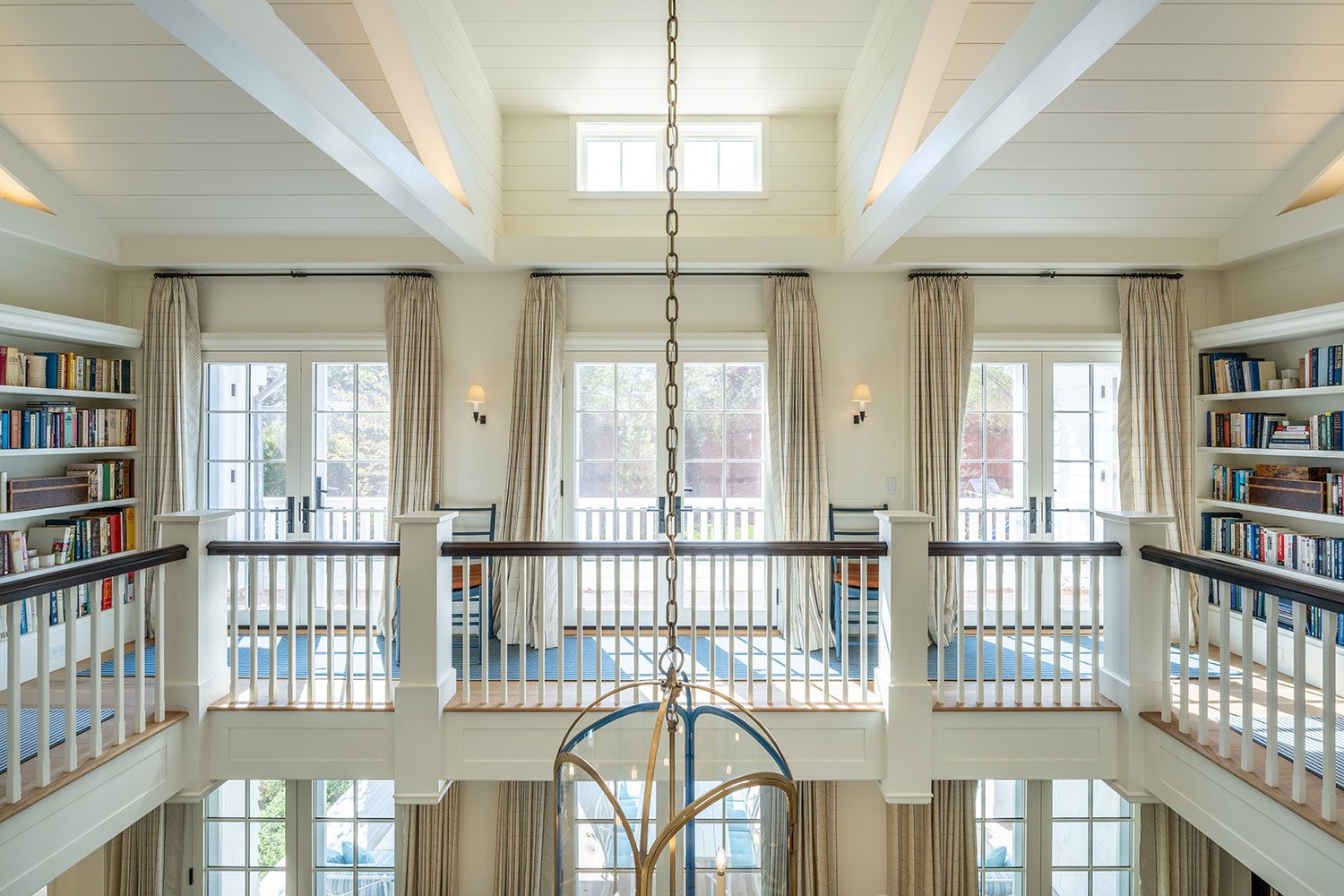 Bright living room with large windows, bookshelves, and a chandelier hanging from the ceiling.