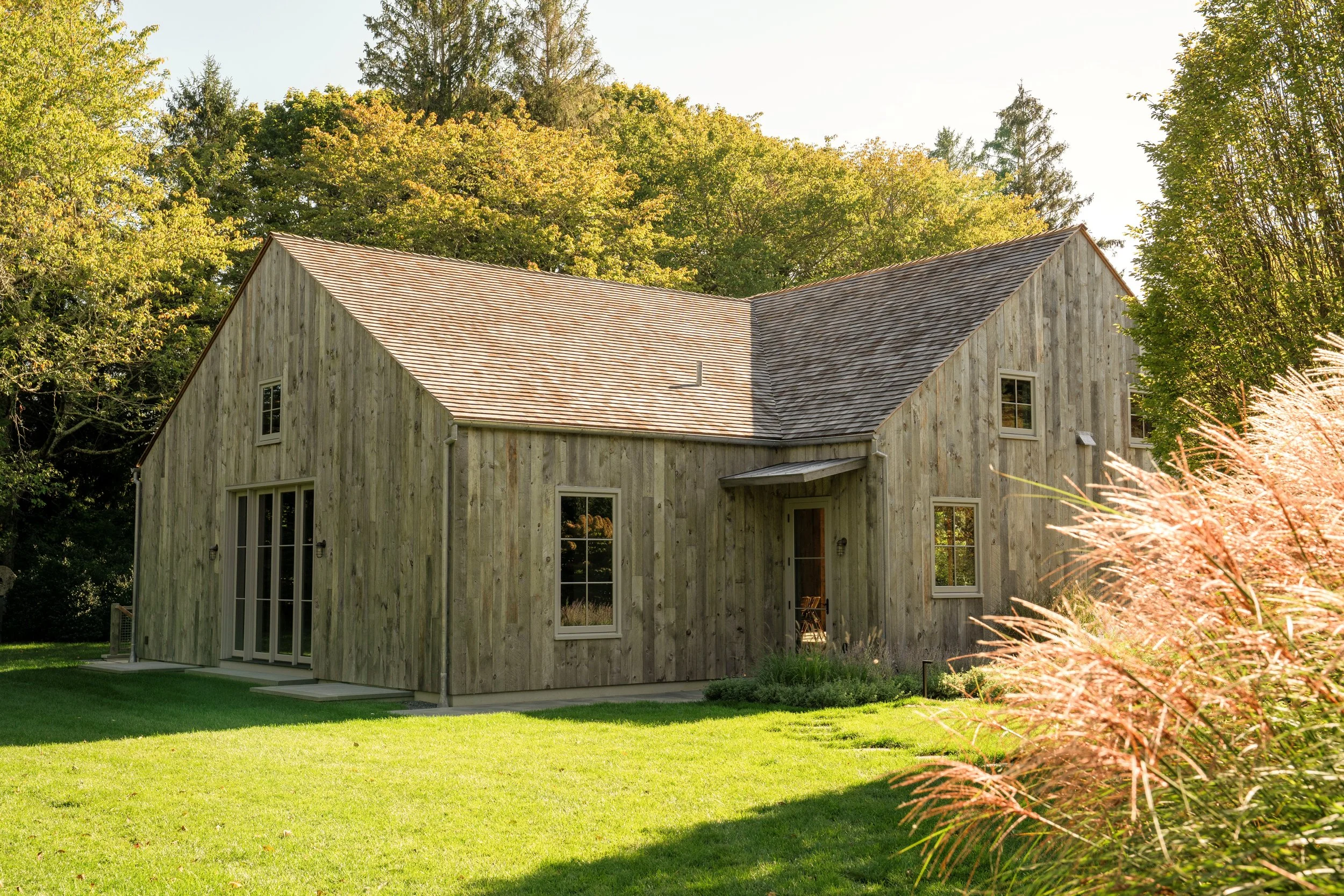 A modern house with wooden siding and a shingle roof, surrounded by green grass and trees.
