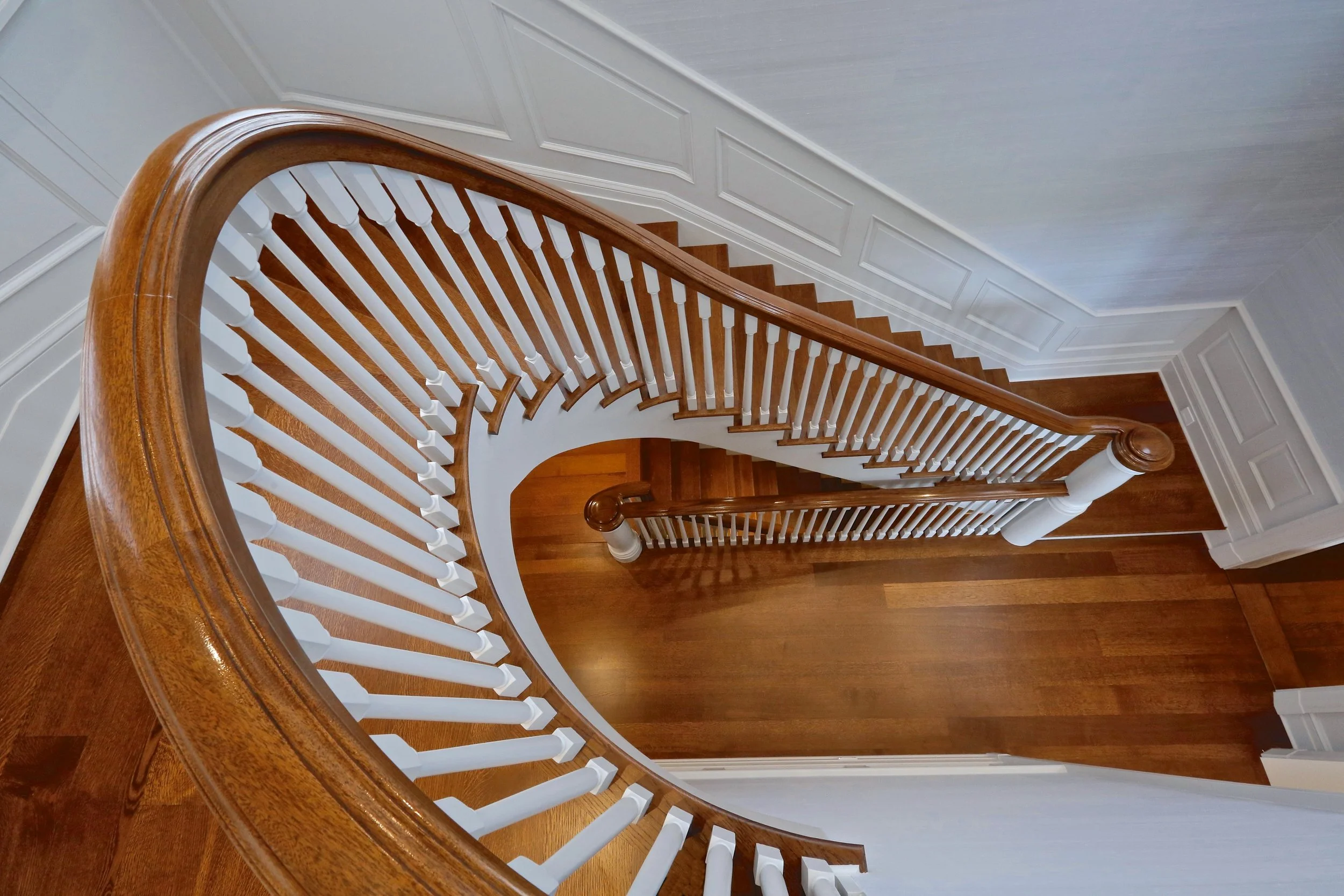 Top-down view of a wooden staircase with white spindles and a curved wooden handrail.