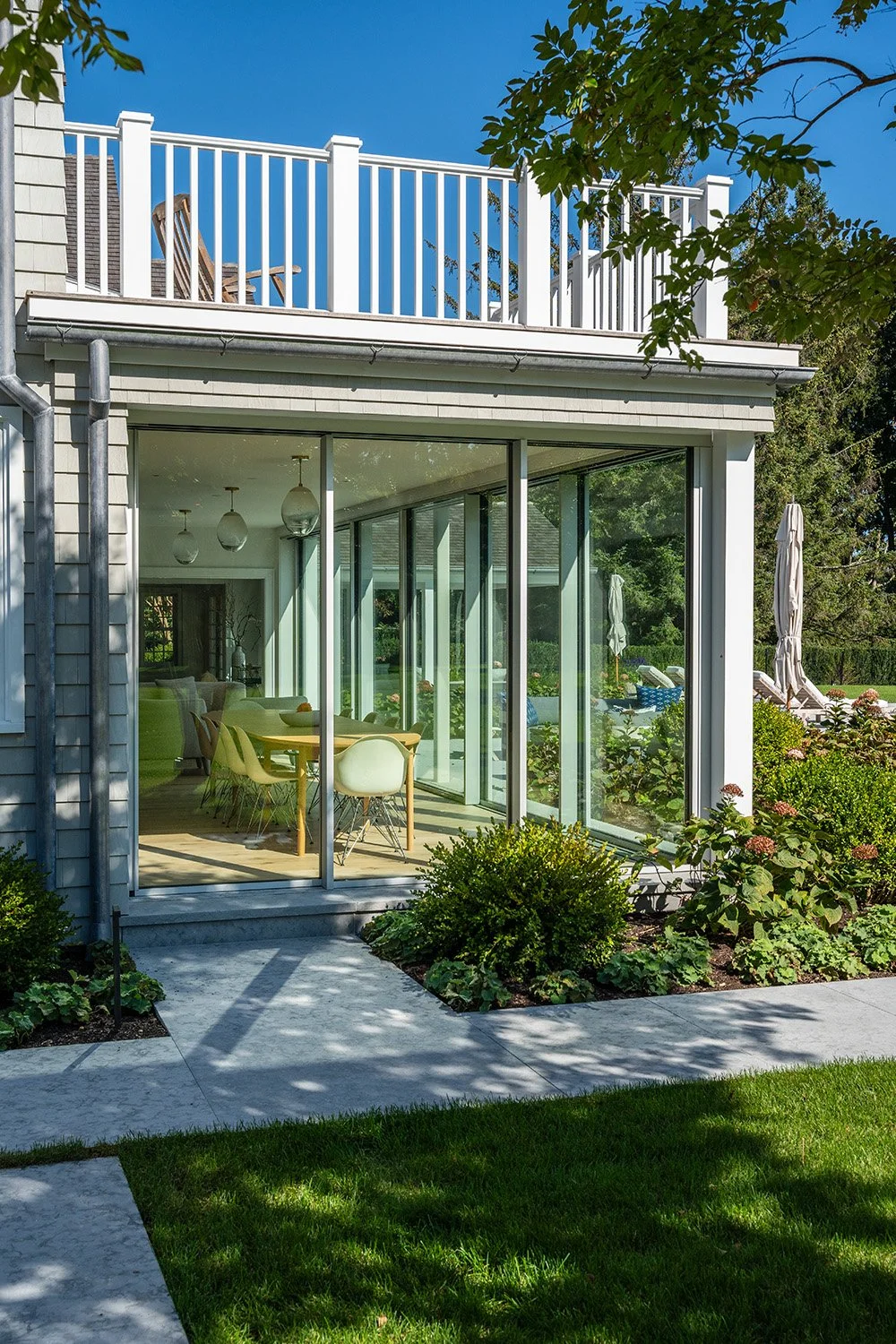 Modern house with large glass sliding doors leading to a patio and garden, featuring outdoor lounge chairs on a backyard lawn.