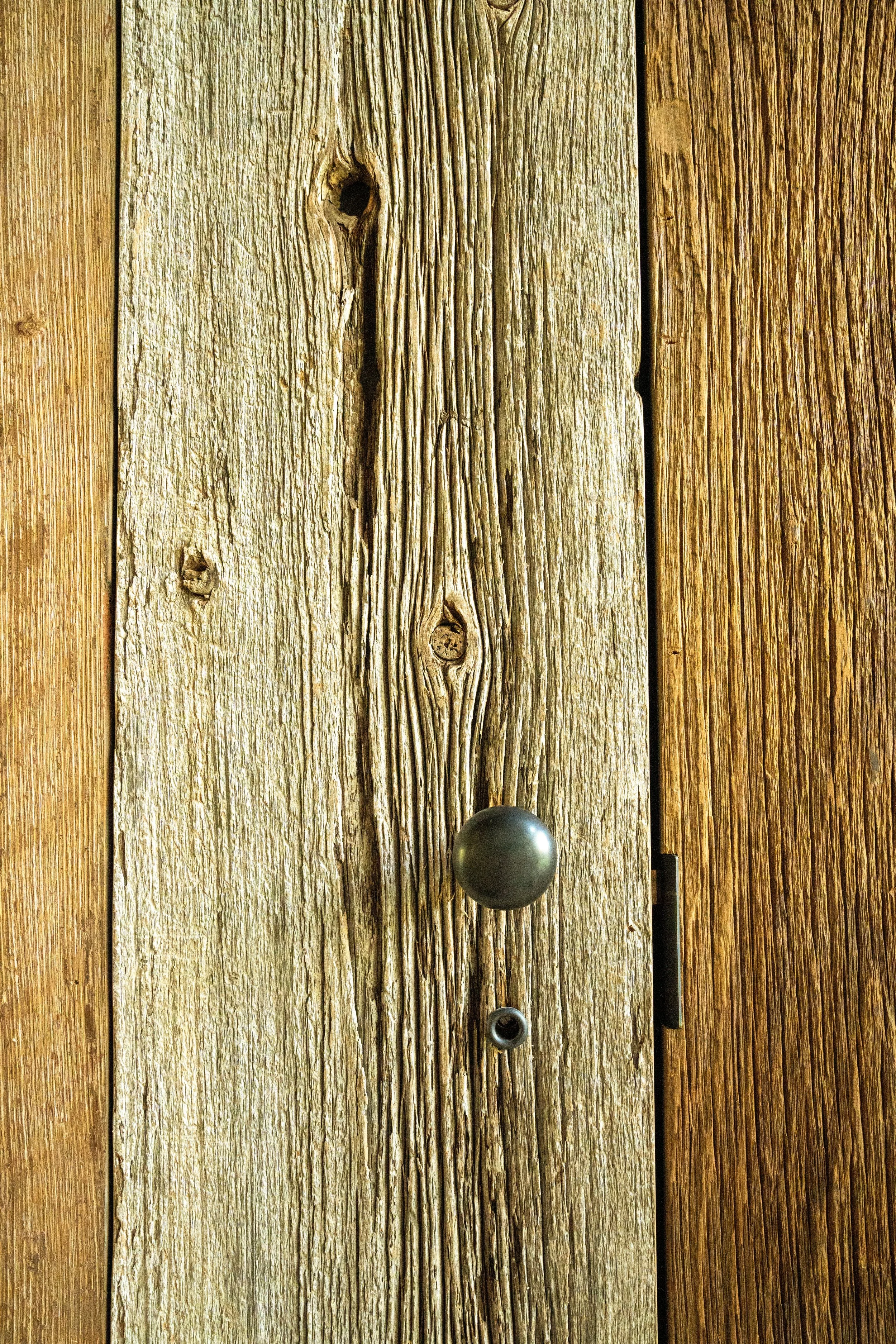Close-up of a weathered wooden door with a round black doorknob and a peephole.