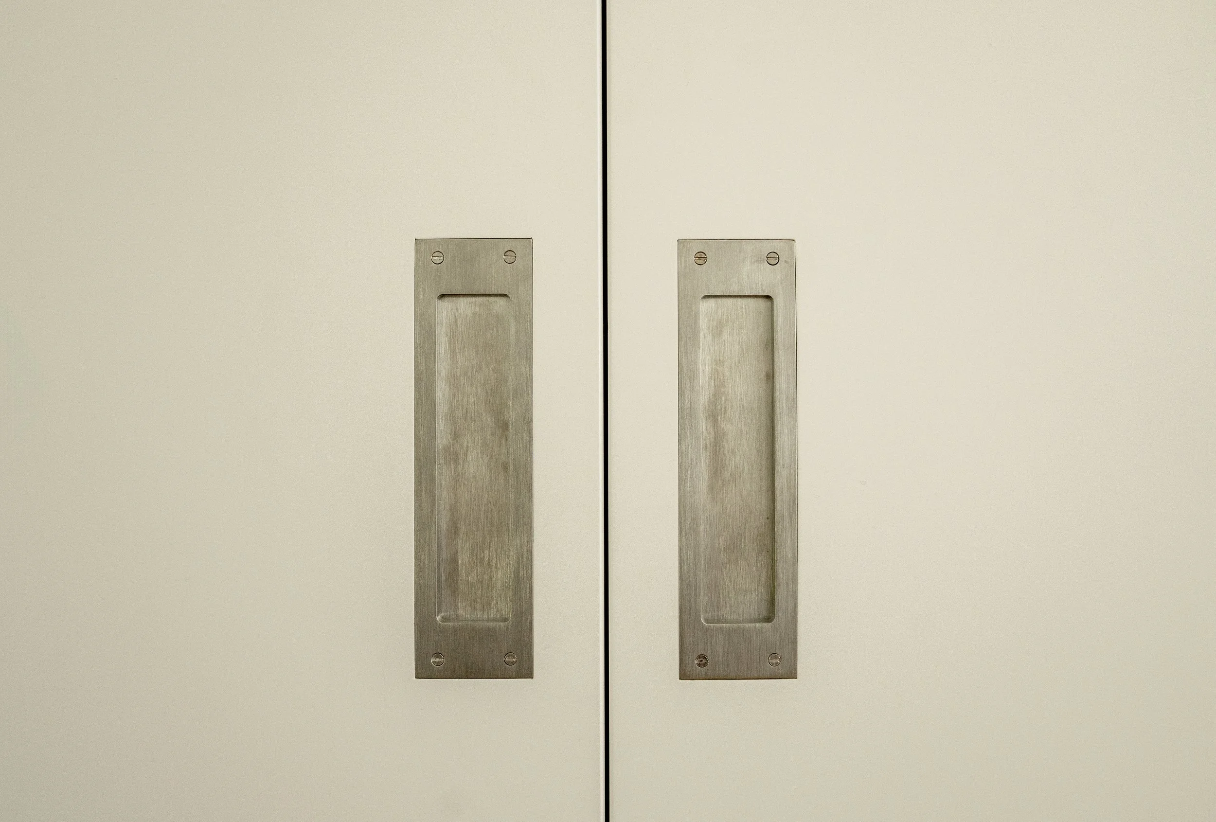 Close-up of two white cabinet doors with metal handles on each door.
