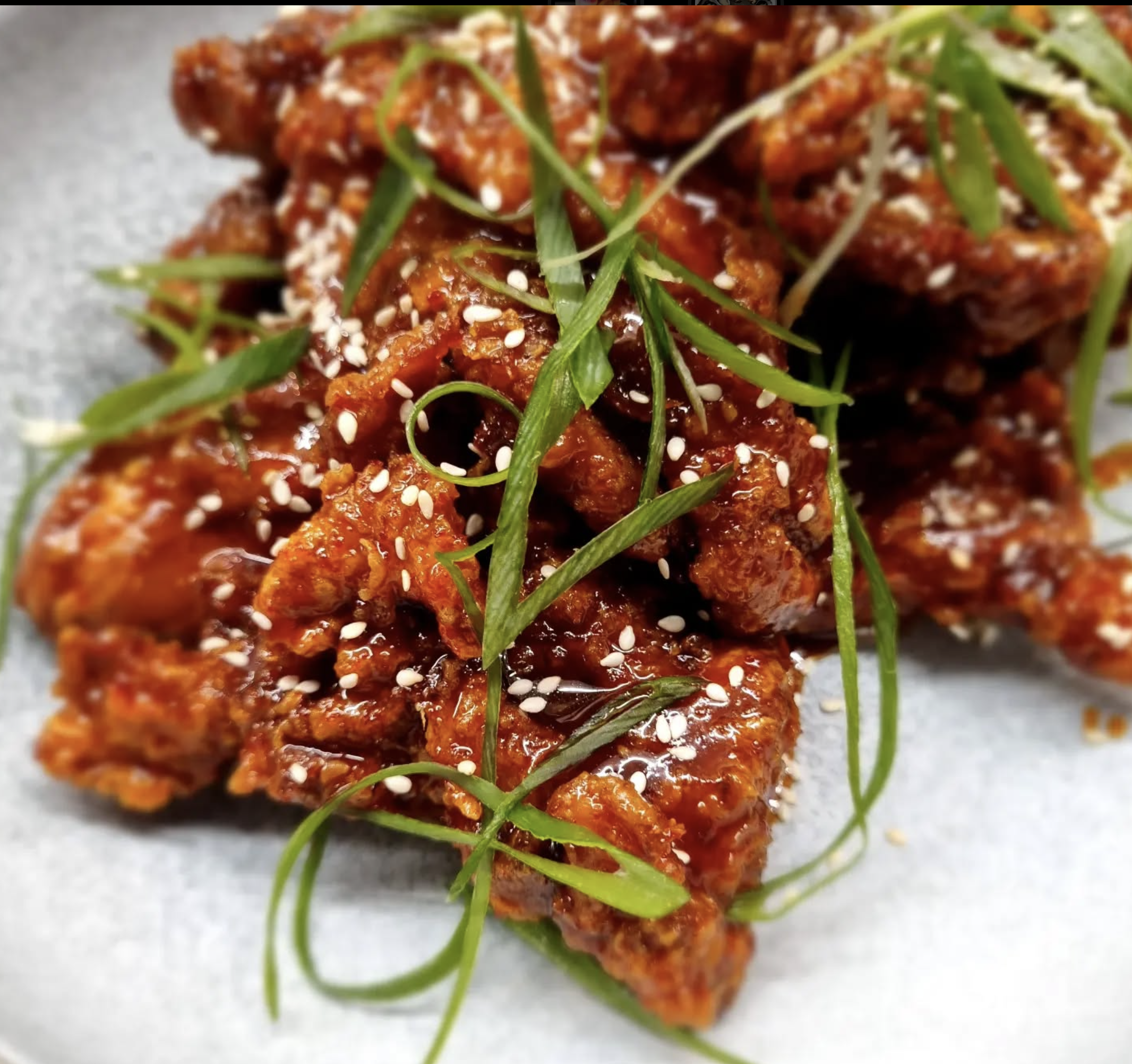 Close-up of spicy glazed chicken wings garnished with sesame seeds and green herbs.
